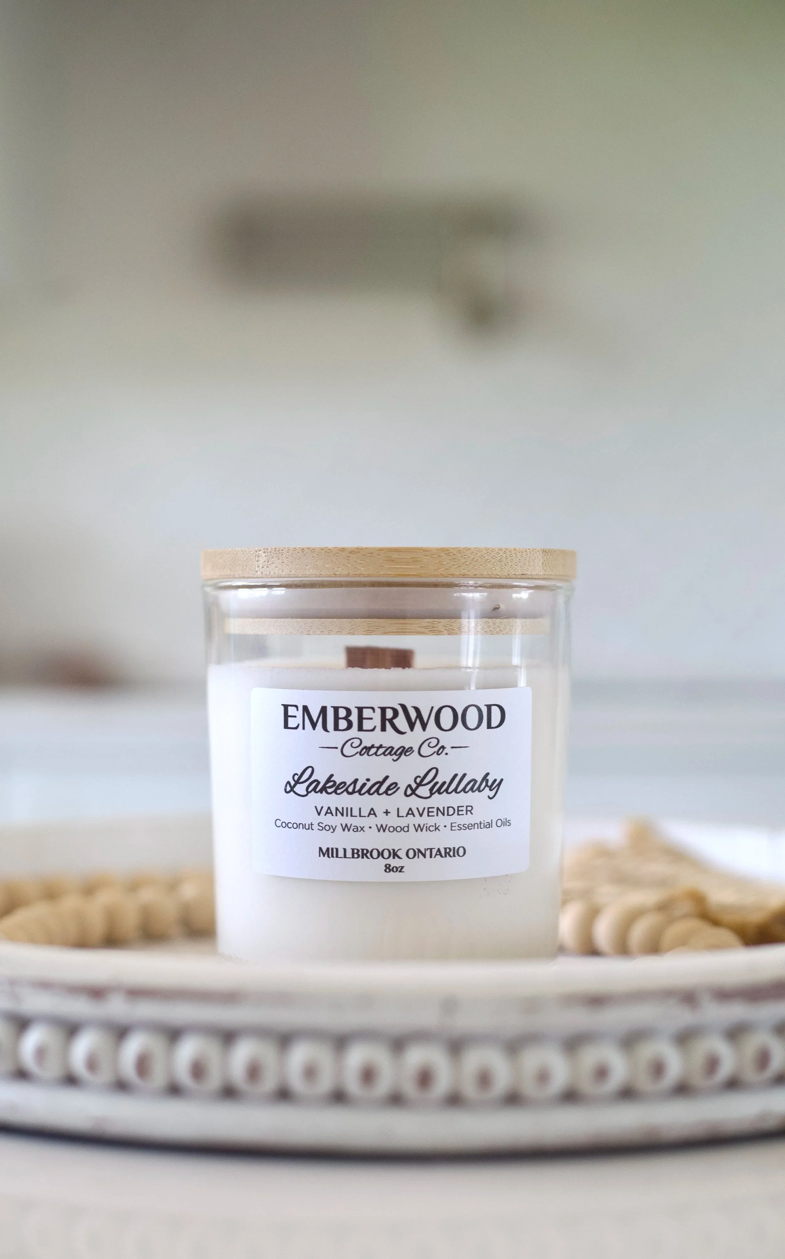 A candle labeled 'Emberwood Cottage Co. Lakeside Lullaby Vanilla + Lavender' on a decorative tray.