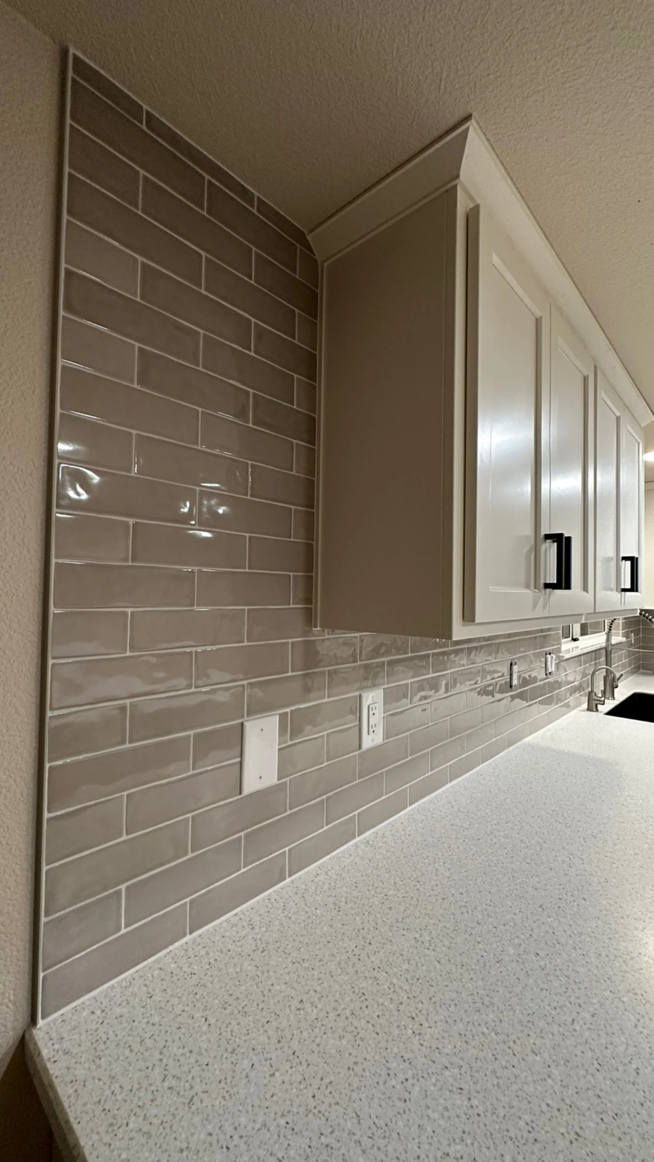 Kitchen countertop with a beige backsplash of subway tiles, white cabinets, and a double electrical outlet.