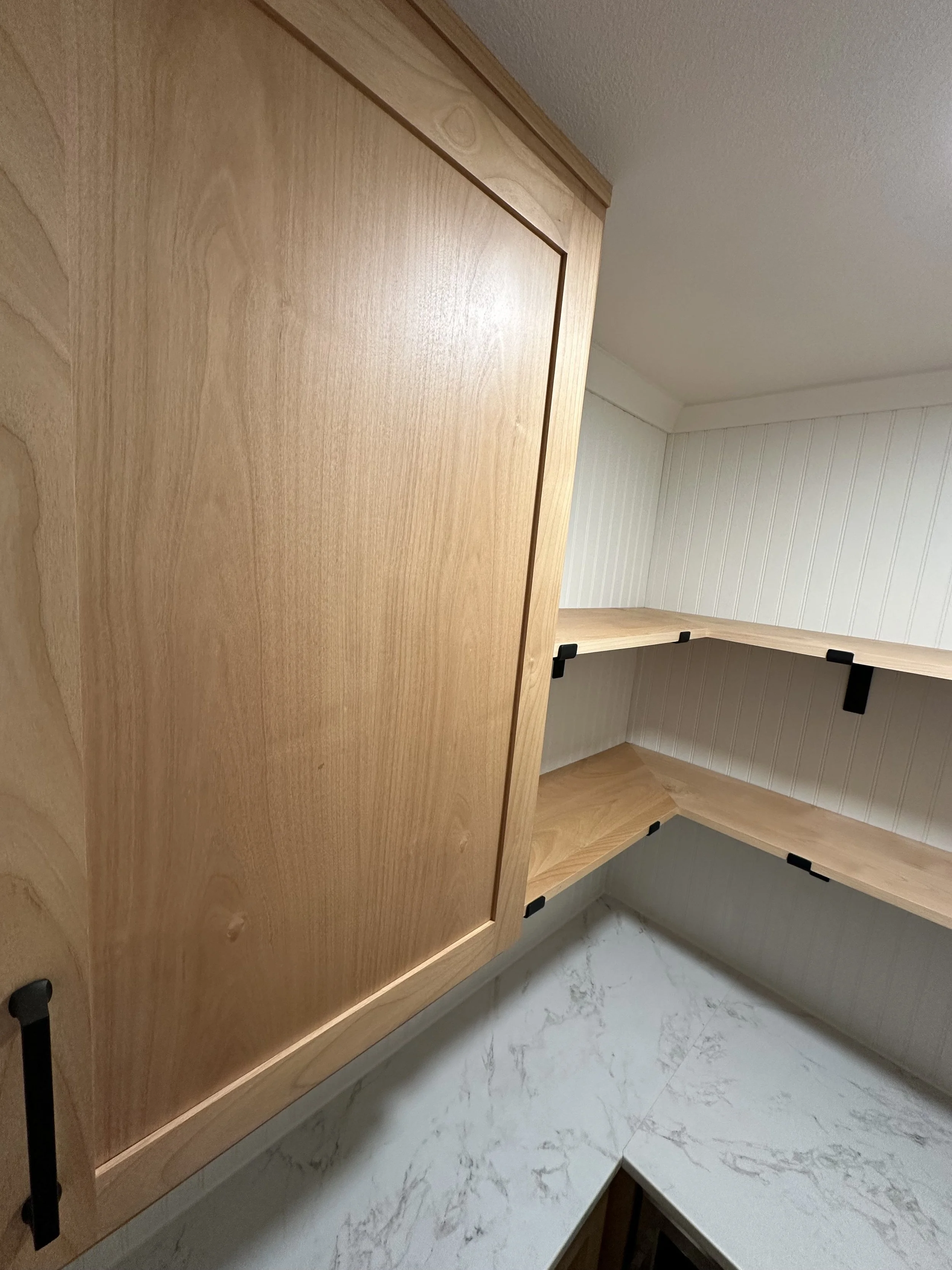 Corner of a wooden cabinet with open shelves and a marble countertop, with a white wall and ceiling in the background.