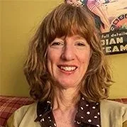 Une femme souriante avec des cheveux bruns ondulés, portant une chemise à pois sur un fond jaune