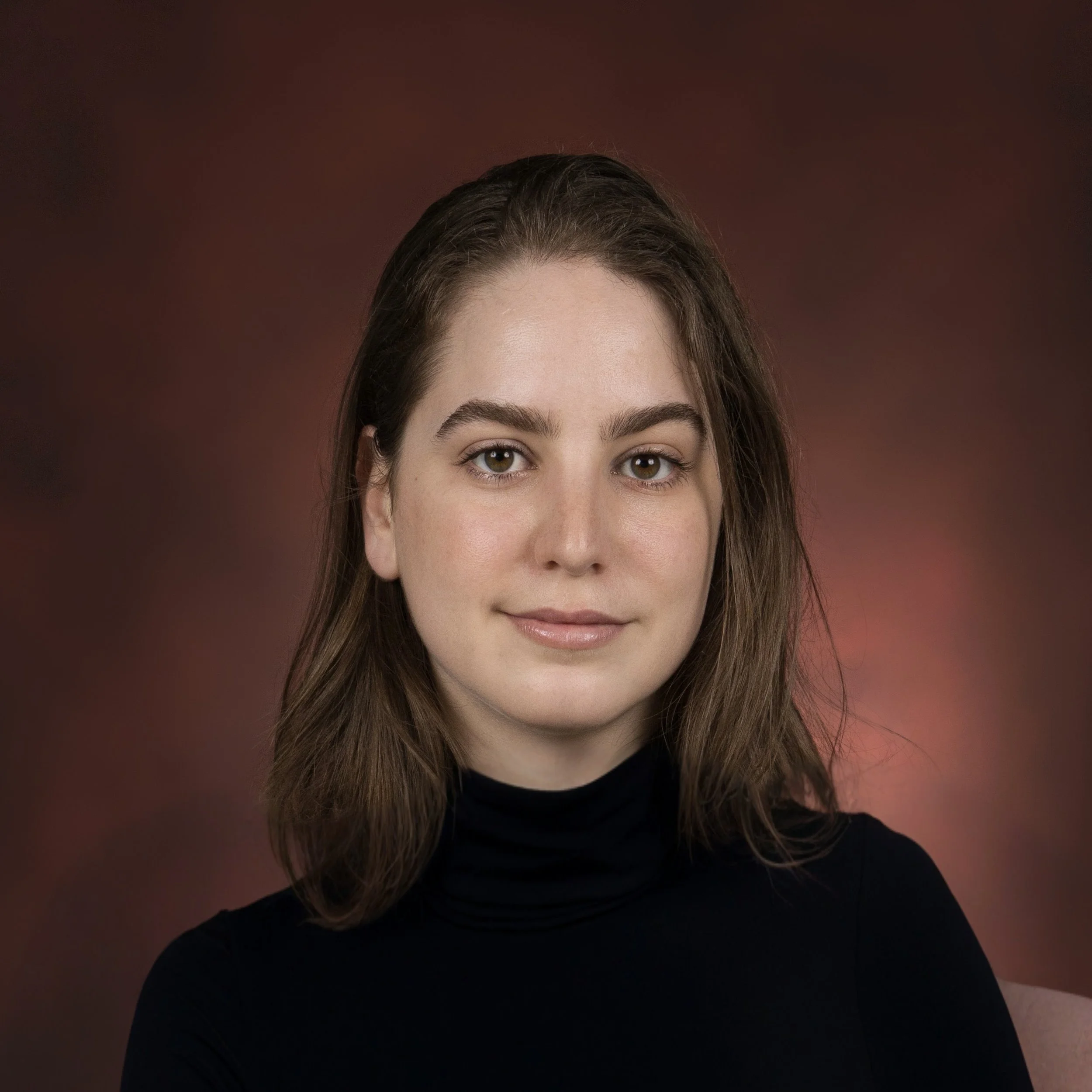 Photo d'une femme aux cheveux bruns, portant un chandail noir, avec un fond marron.