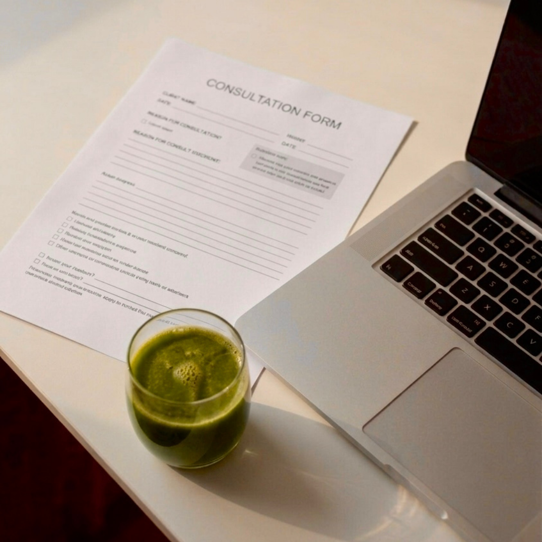 Consultation form, laptop, and a glass of green juice on a white table.