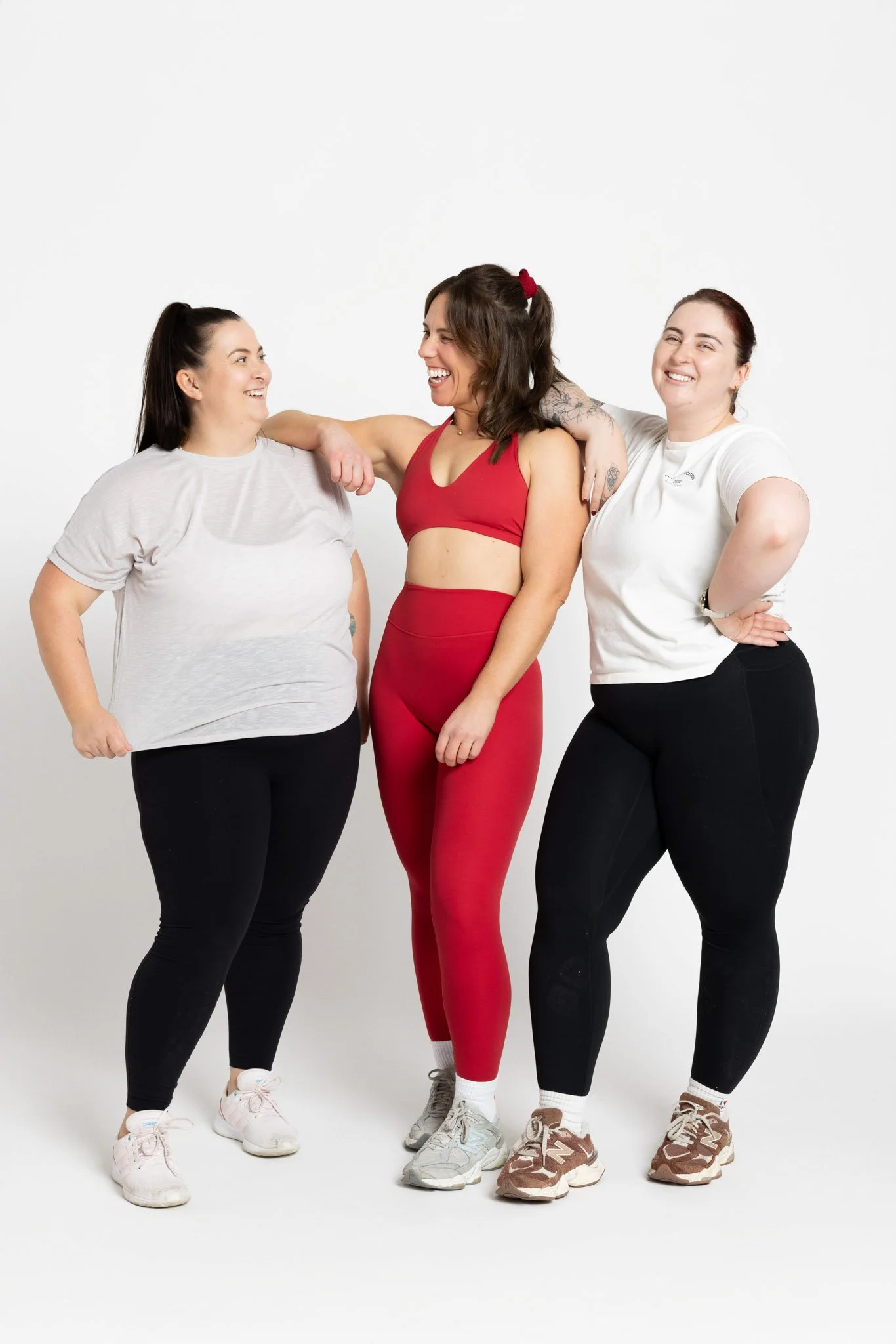 Three women standing together smiling and laughing against a plain white background.