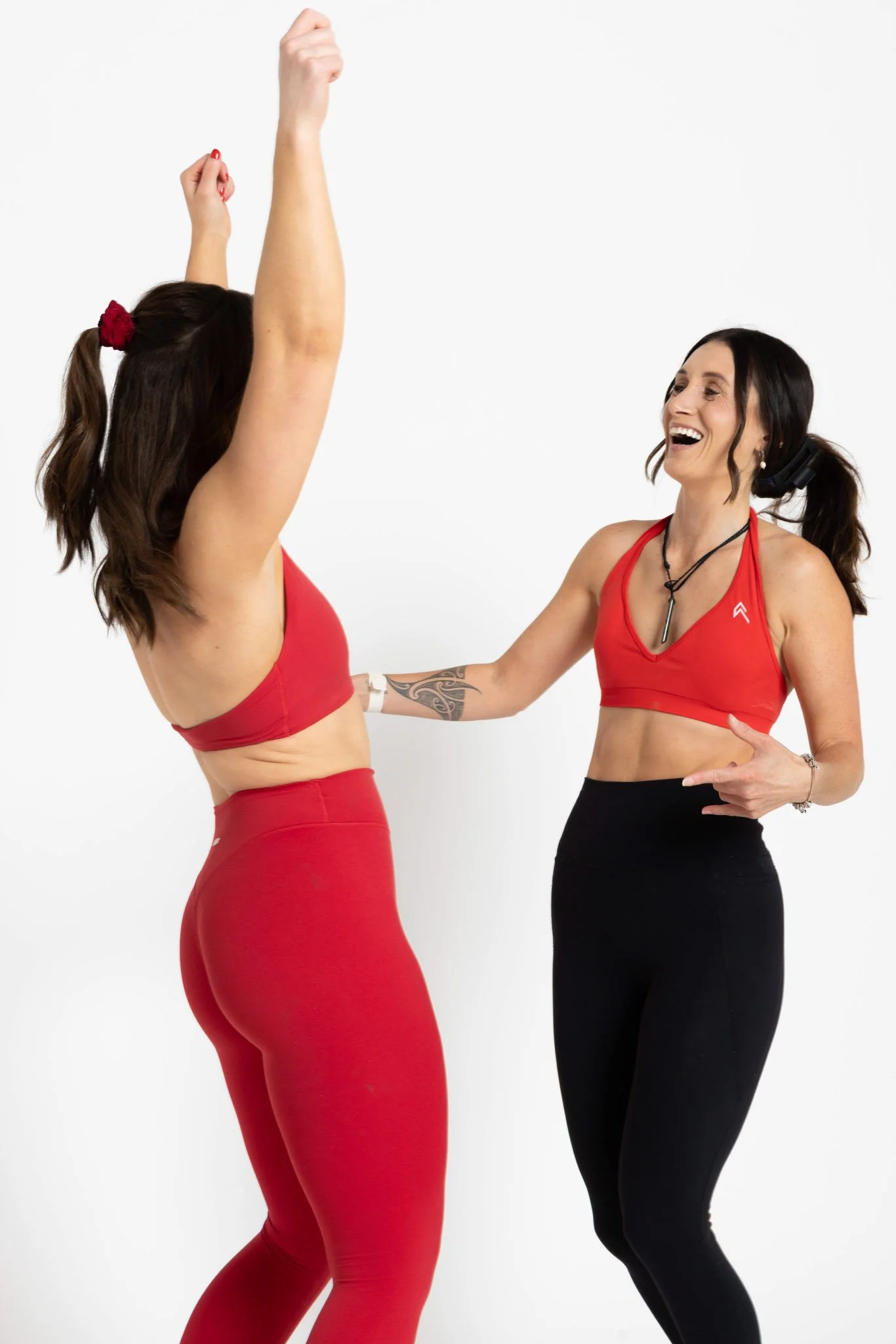 Two women in athletic clothing cheer and laugh together against a plain white background.