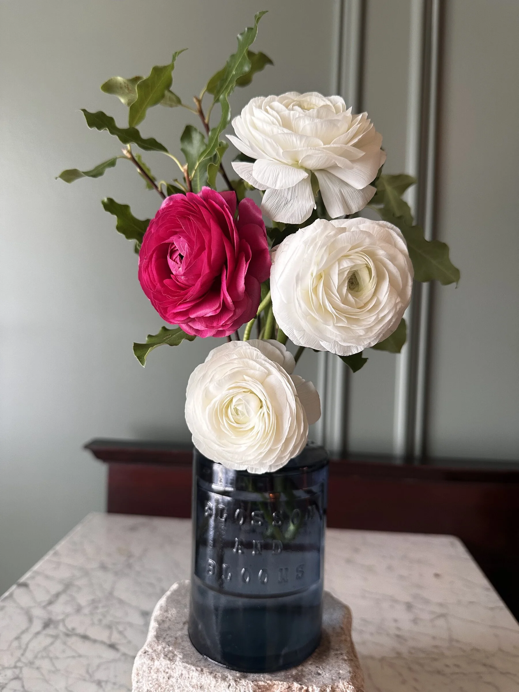 A bouquet of white and pink ranunculus flowers in a glass vase on a marble table.