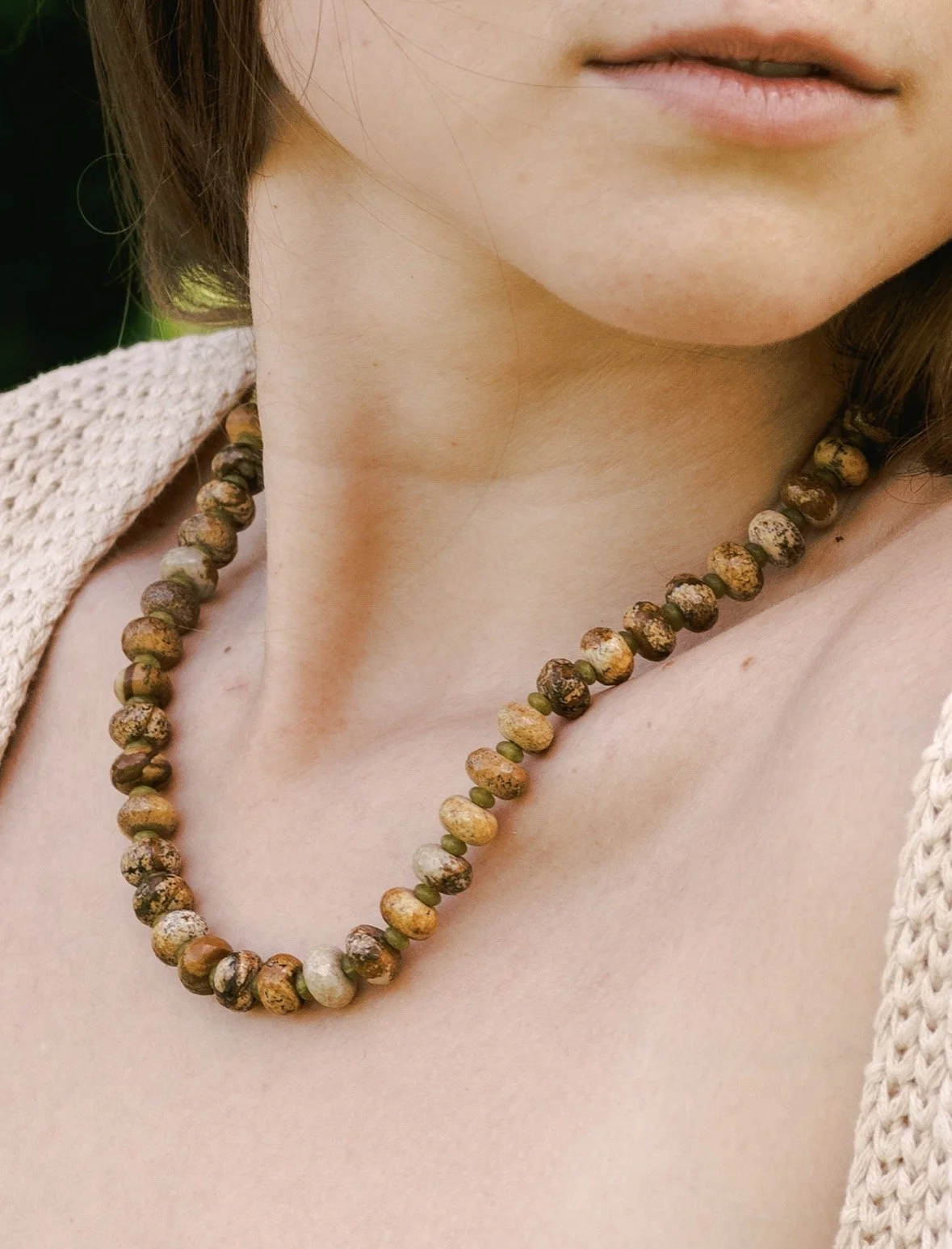 Close-up of a woman's lower face, neck, and upper chest, showing a beaded necklace made of multicolored round stones.