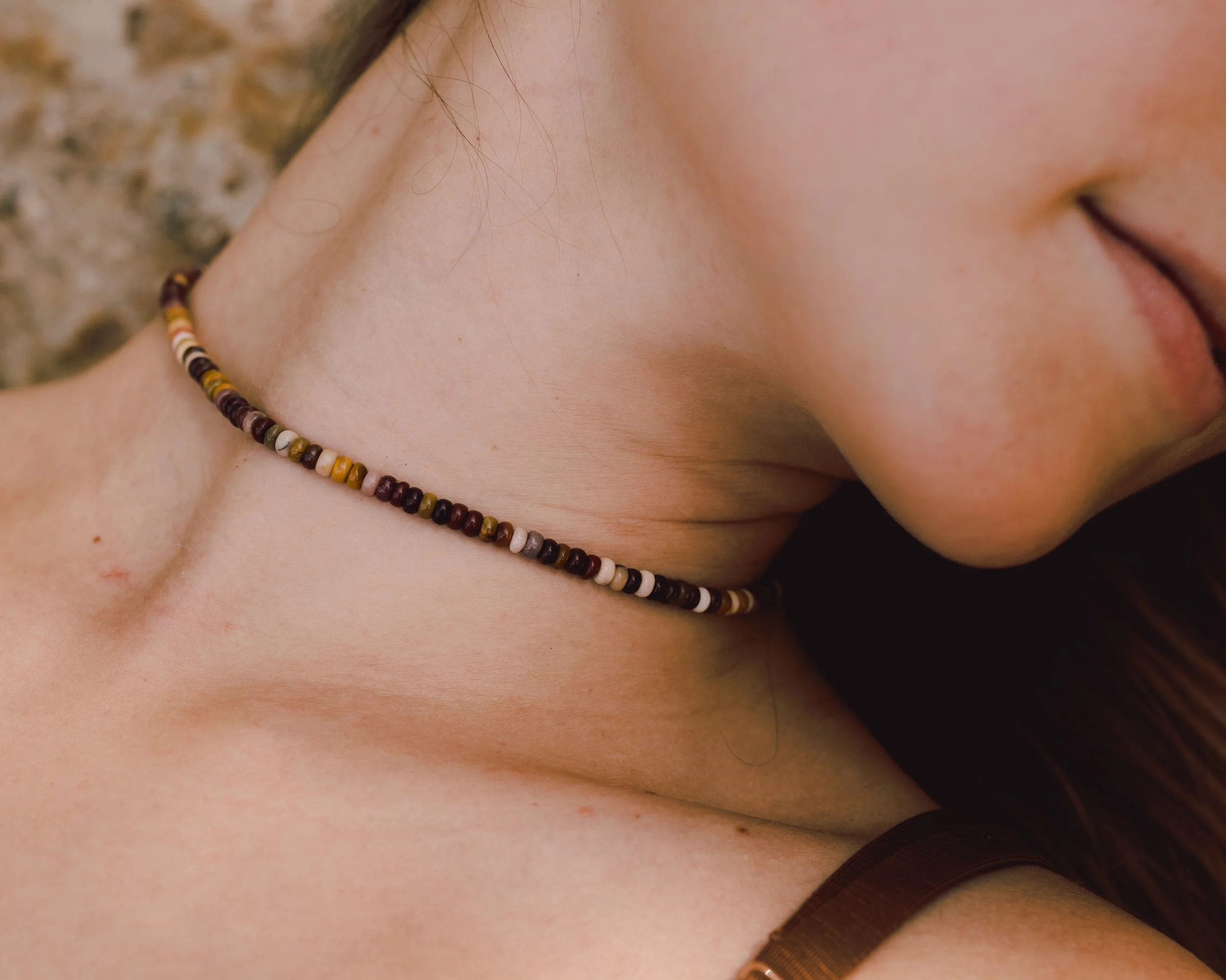 Close-up of a woman's neck and profile, wearing a beaded necklace, with smooth skin and a hint of a smile.