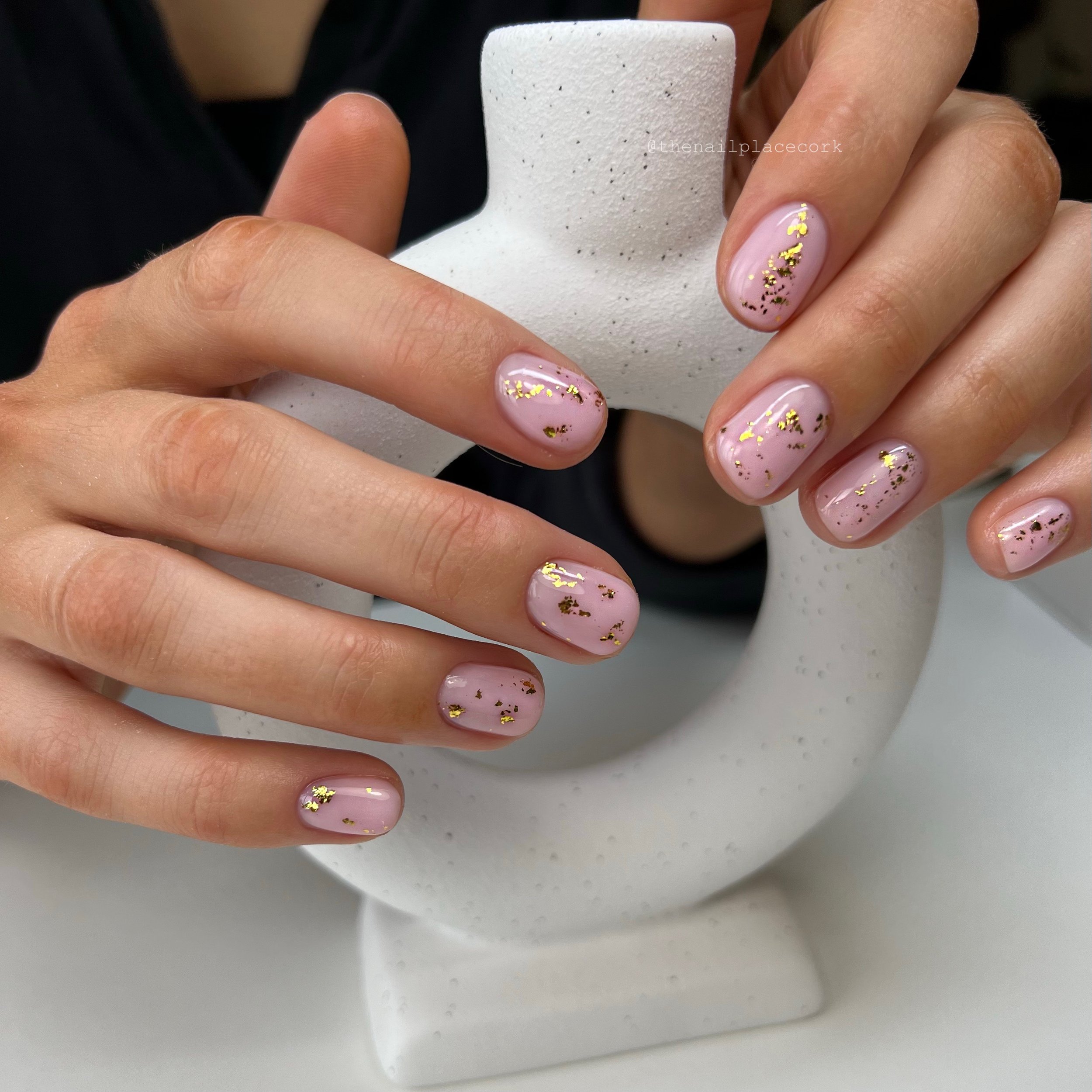 Close-up of hands with pink nail polish and gold leaf details, holding a white ceramic object with a hole in the center.