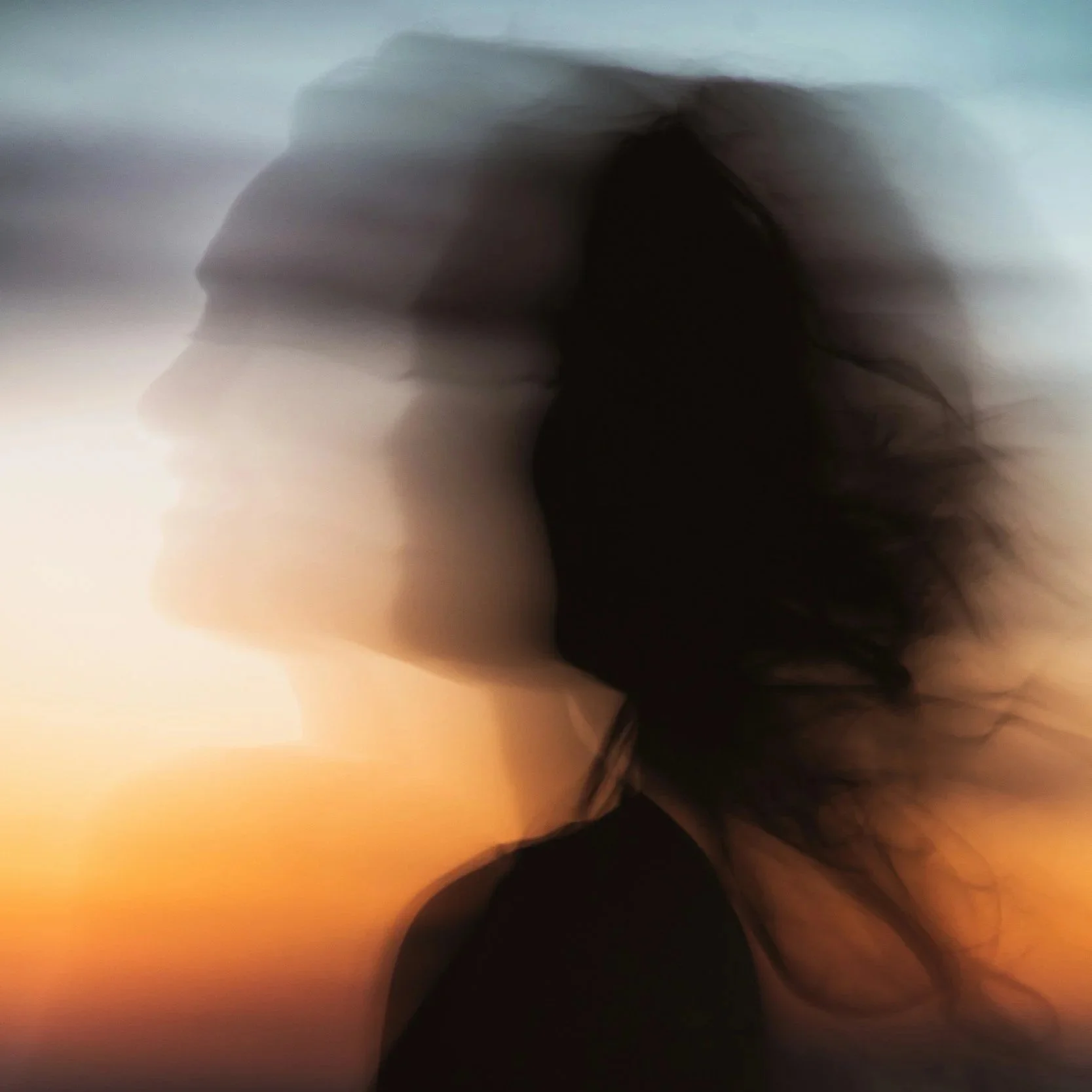 Blurred silhouette of a woman's profile with flowing hair against a sunset sky.