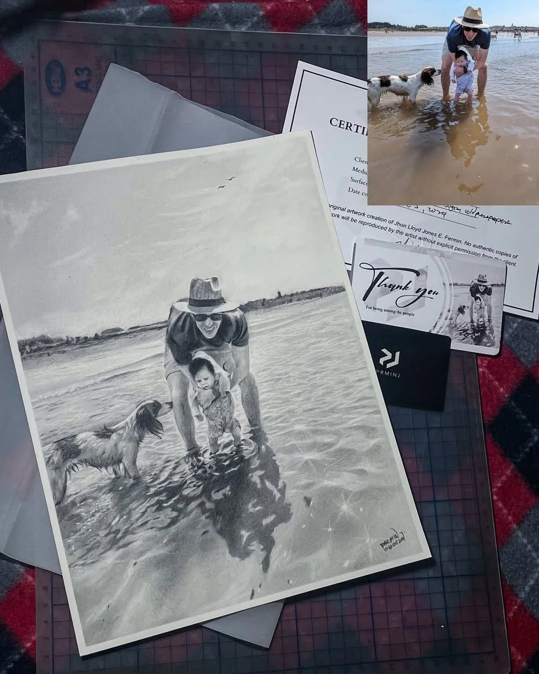 A collection of papers, including a grayscale drawing of a woman, a child, and two dogs at the beach, with an actual photograph of a woman and a child playing in the shallow water at the beach in the background.