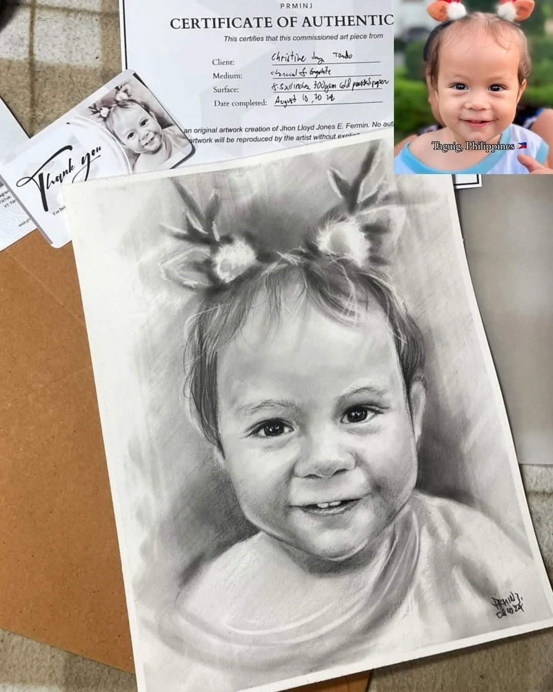 A realistic black-and-white charcoal or graphite portrait drawing of a smiling young child with Christmas reindeer antlers on her head. There is a smaller color photo of the same child in the upper right corner with a flower headband, labeled Taguig,