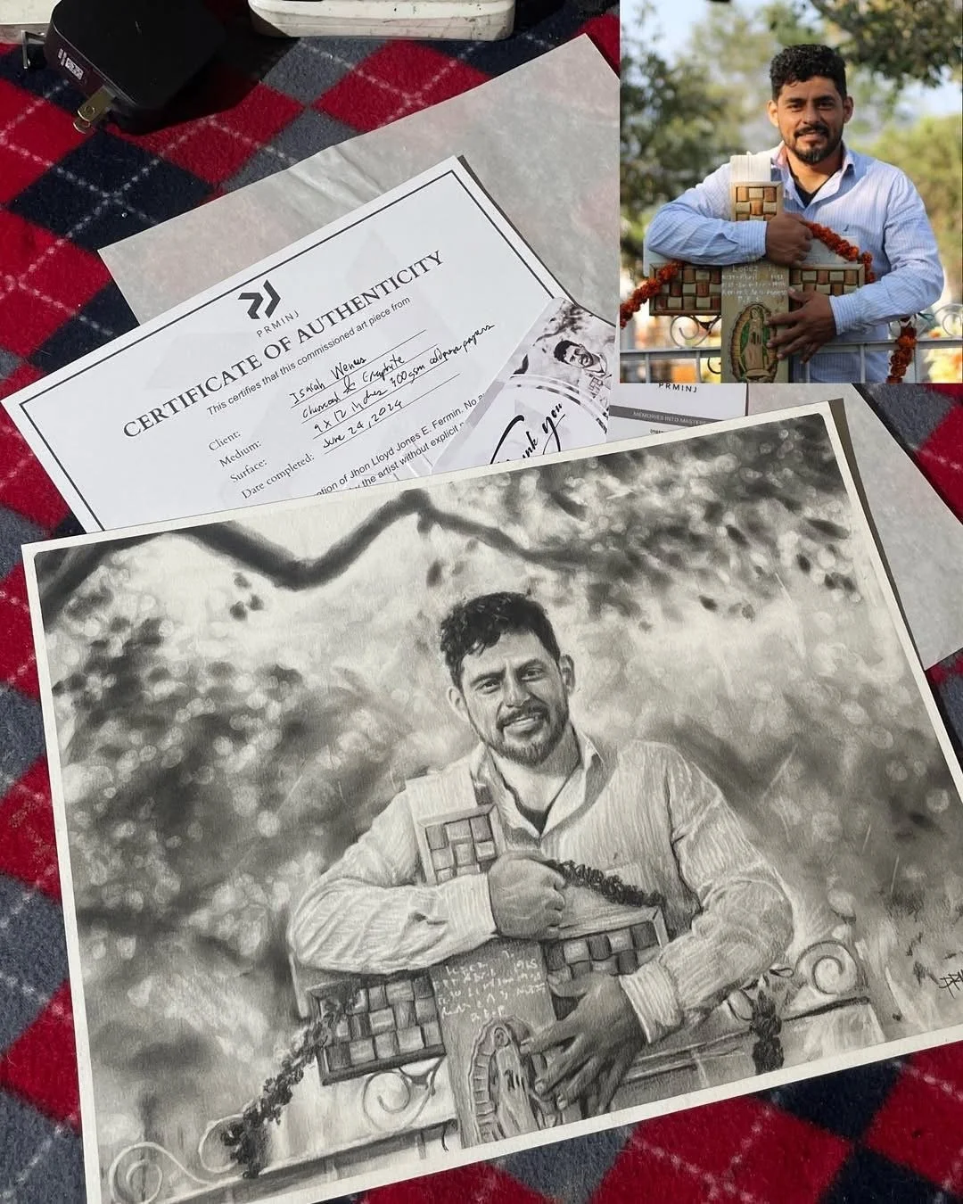A black and white sketch of a man holding a puzzle piece, with a background of trees and clouds, displayed on a table alongside a printed certificate of authenticity and a smaller photo showing the same man holding the original artwork outdoors.