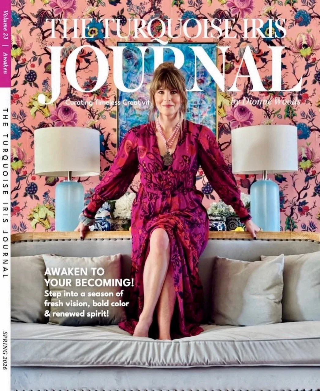 The Spring 2026 magazine cover of The Turquoise Iris Journal featuring a woman, Dionne Woods in a magenta dress elegantly sitting on a beige sofa, with a floral wallpaper background, two white lamps and pillows.