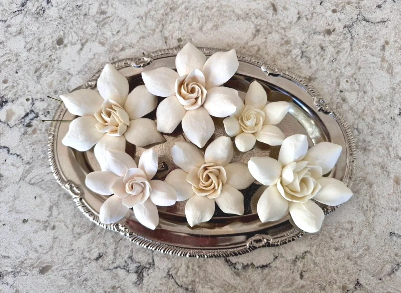 Realistic-looking gardenia hair flowers made of air-dry clay sitting on a silver tray atop a marble surface.
