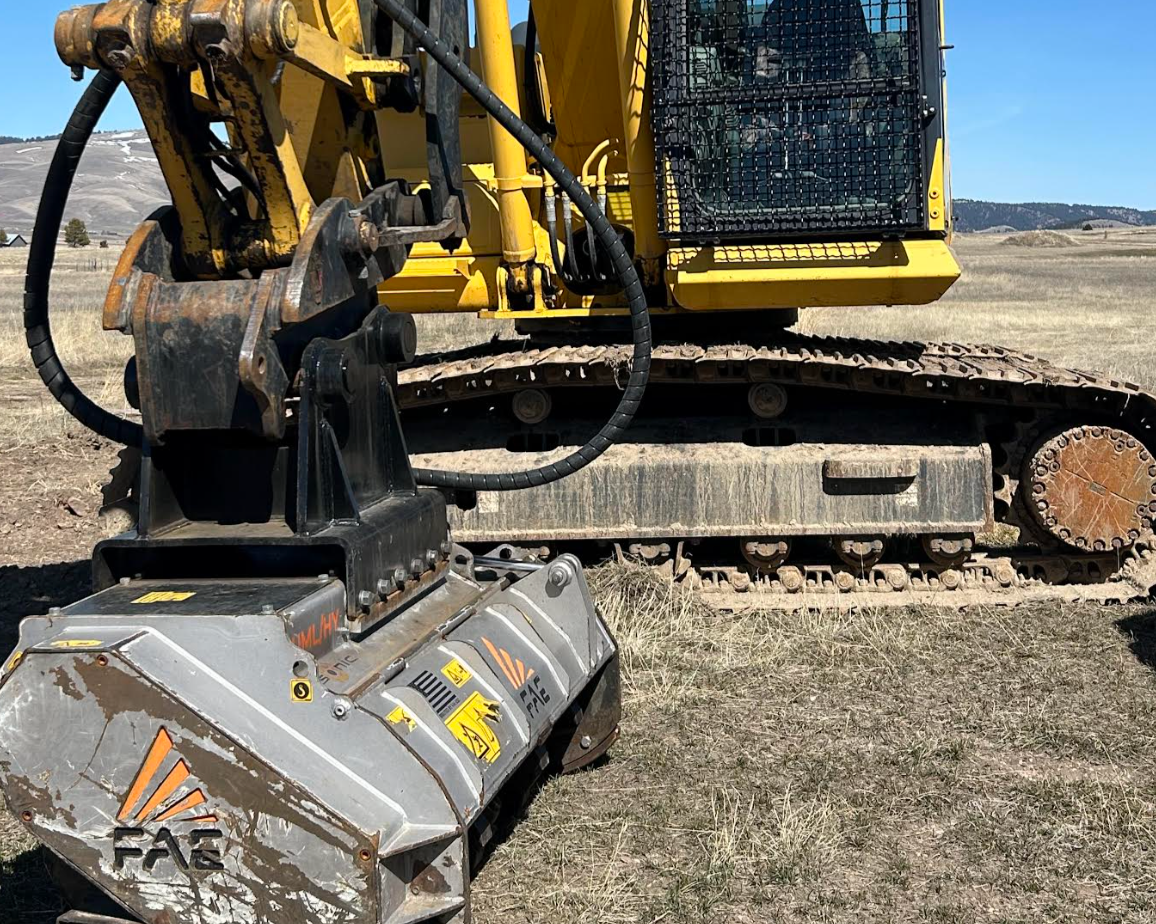 Close-up of a yellow excavator with black tracks working on a dirt field, under a clear blue sky.