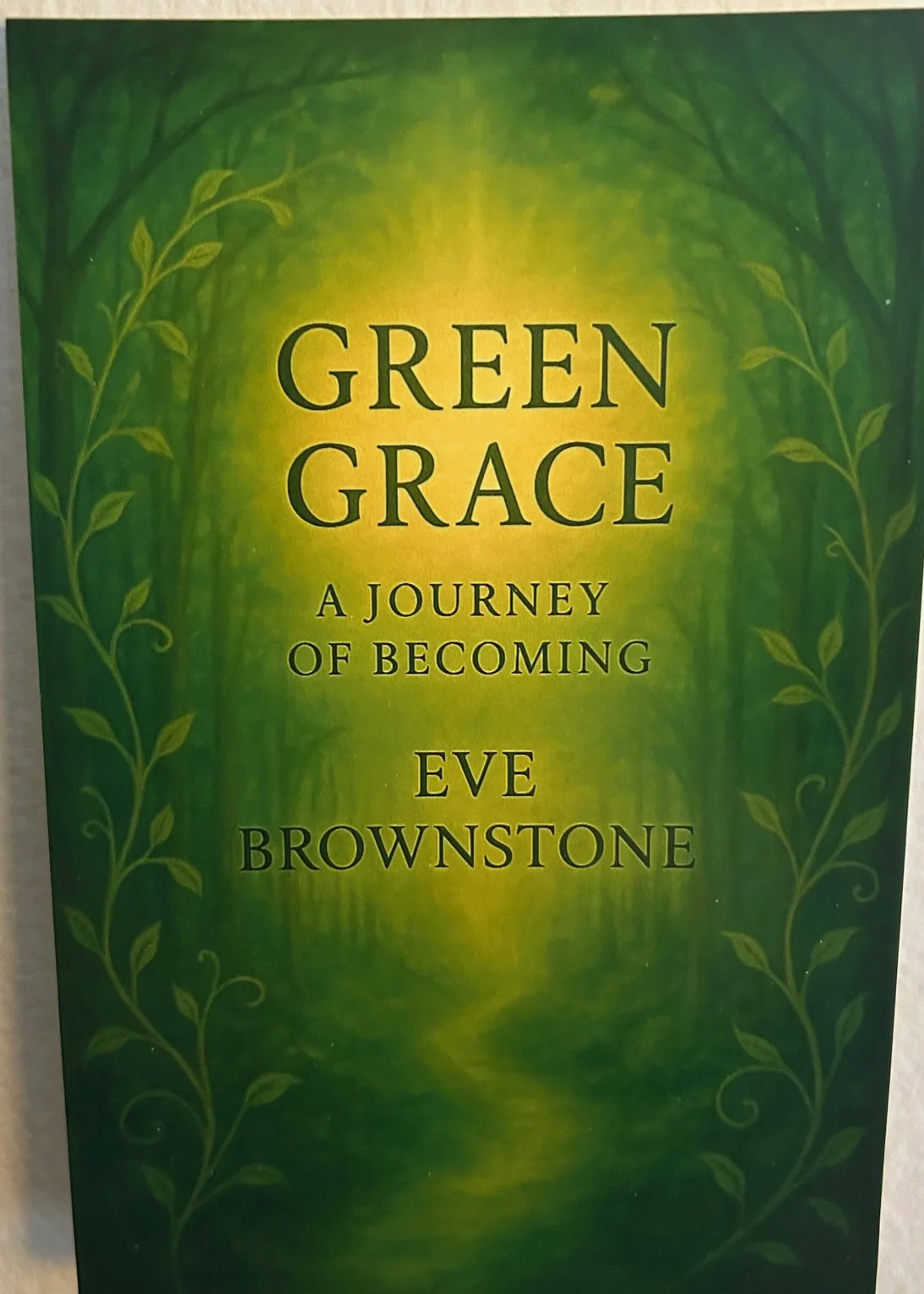 Book cover titled 'Green Grace: A Journey of Becoming' by Eve Brownstone, featuring a green and yellow background with a forest scene and decorative leaves.