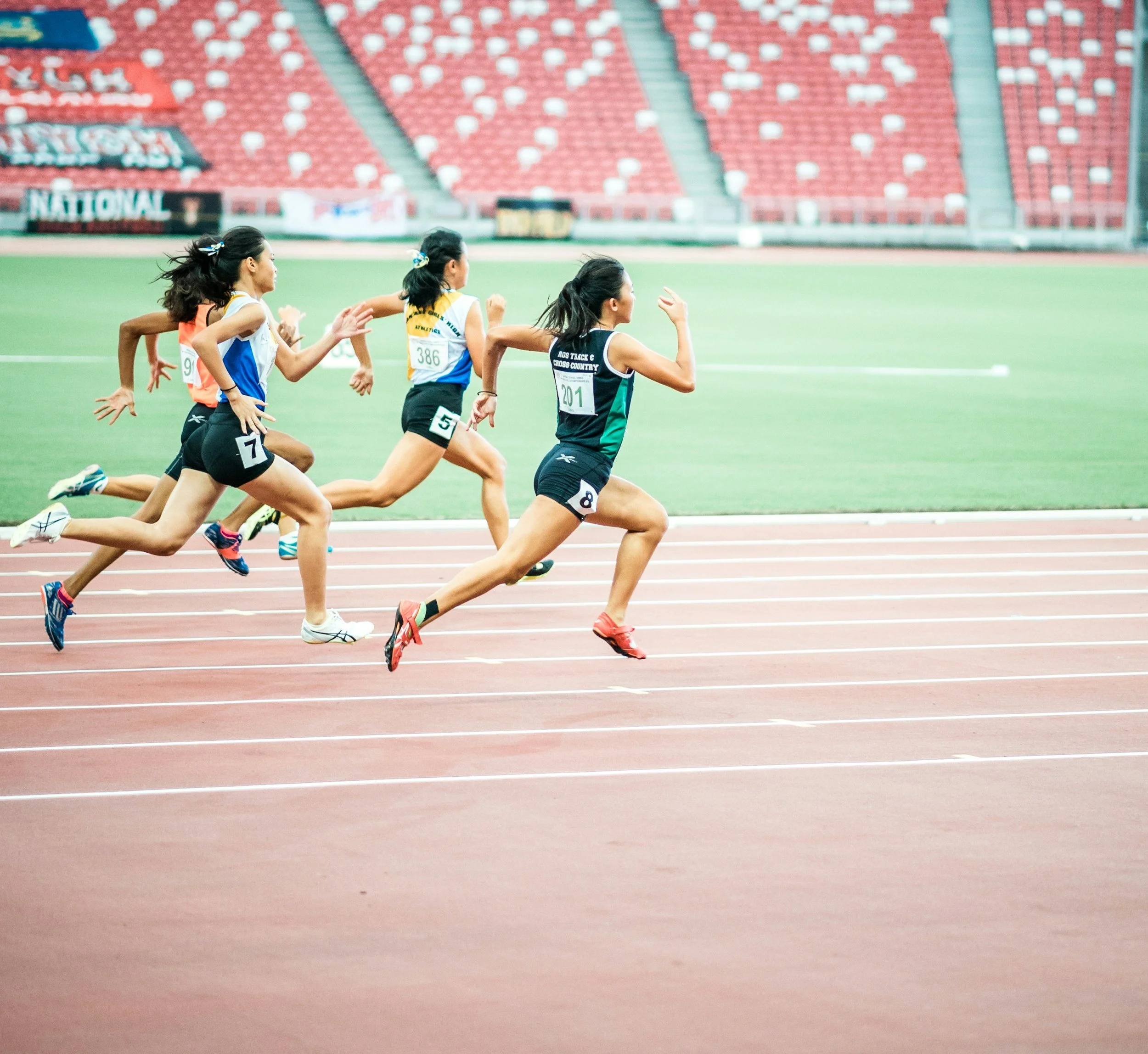 Female athletes running a race on a track in a stadium.