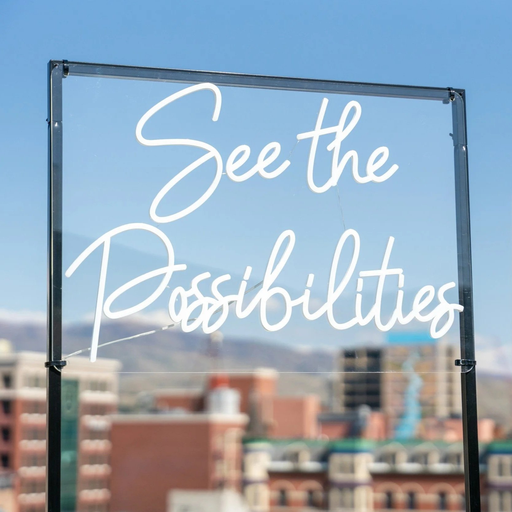 Neon sign reading 'See the Possibilities' against a city skyline and mountains in the background.