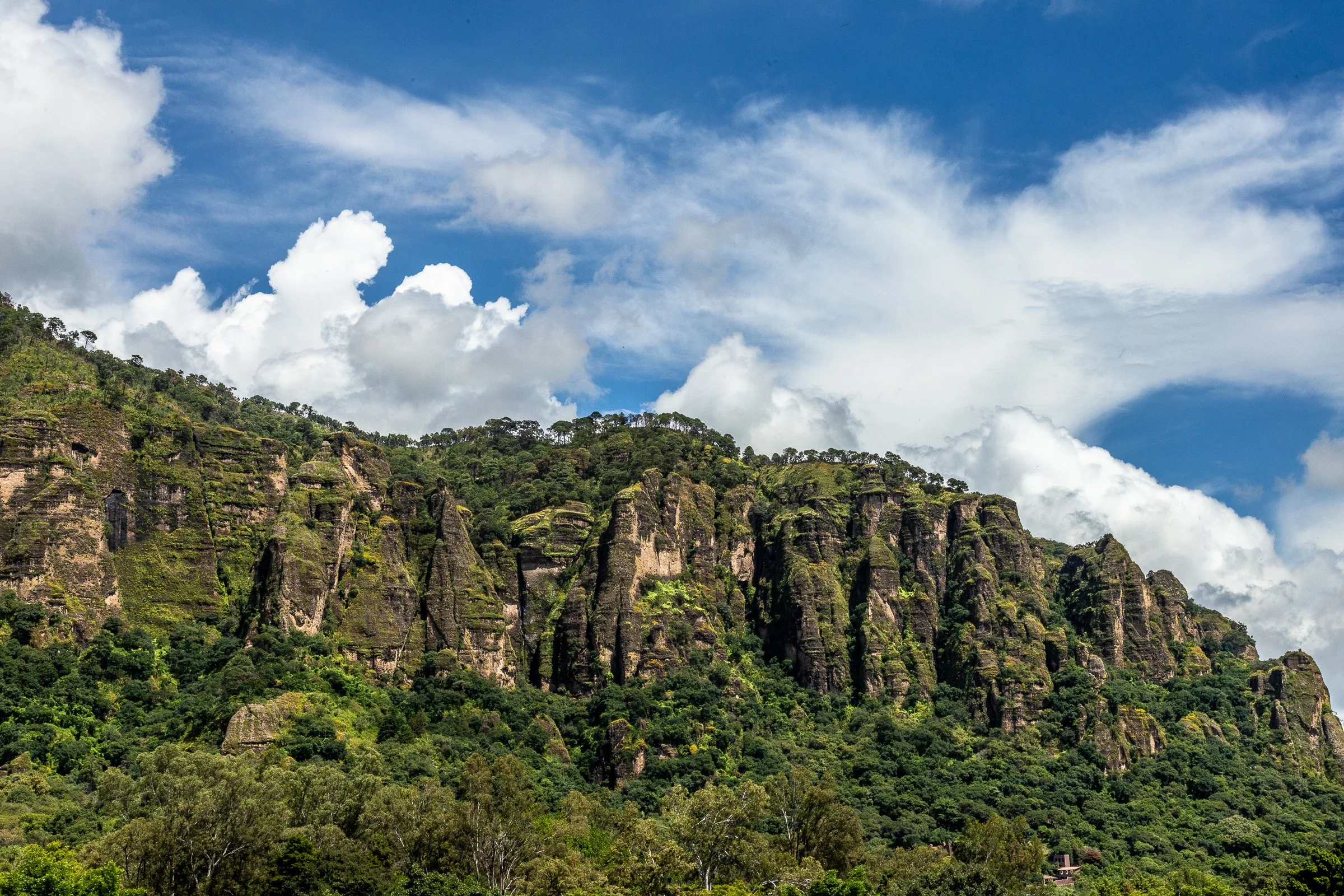 Montaña cubierta de vegetación con formaciones rocosas y un cielo azul con nubes.