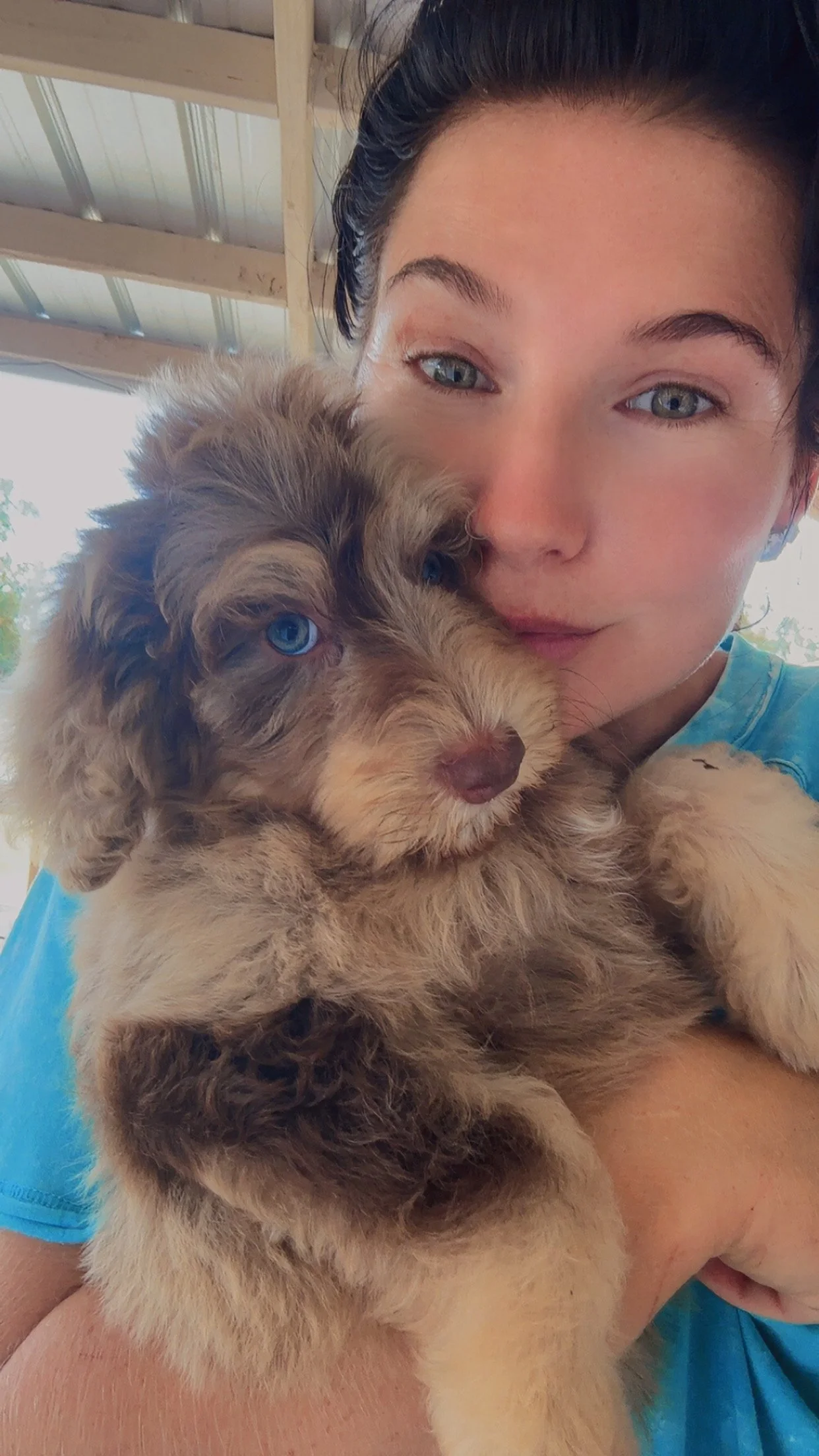 A woman holding a fluffy puppy with blue eyes, indoors near a metal roof structure.