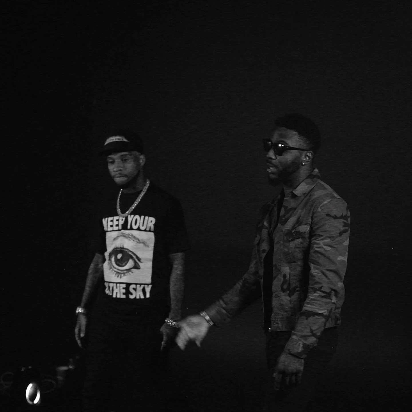 Two young men in dark clothing and sunglasses standing in a dark environment.