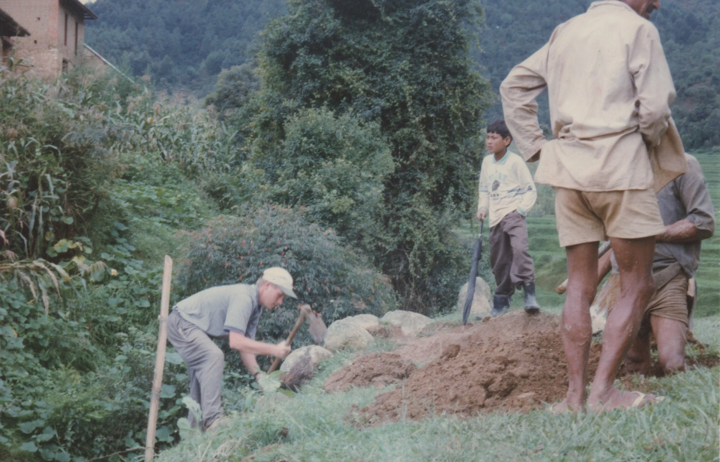 John digging a hole for tree planting using a kuto (a small pick axe)