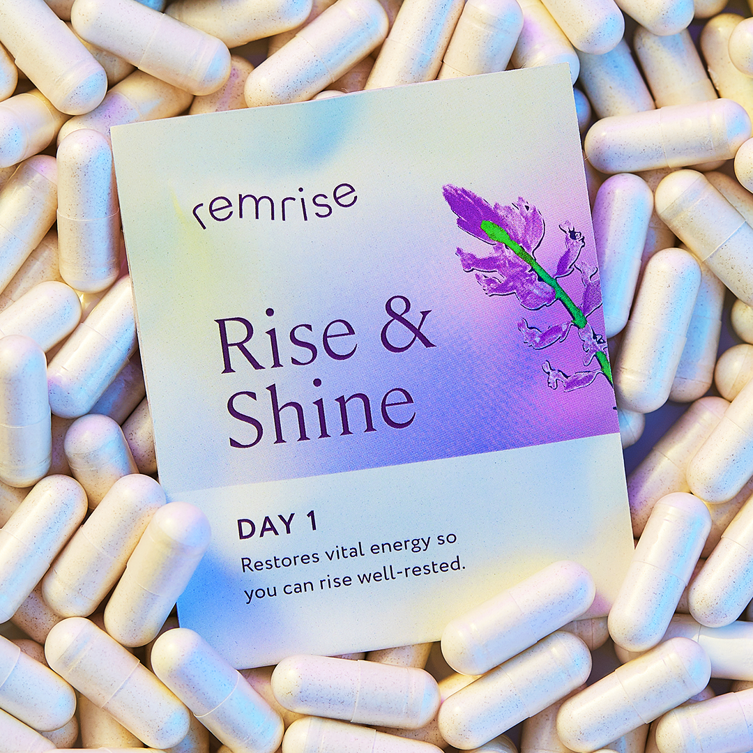 A packet labeled 'Rise & Shine' surrounded by white capsules, with a purple flower illustration on the packet.