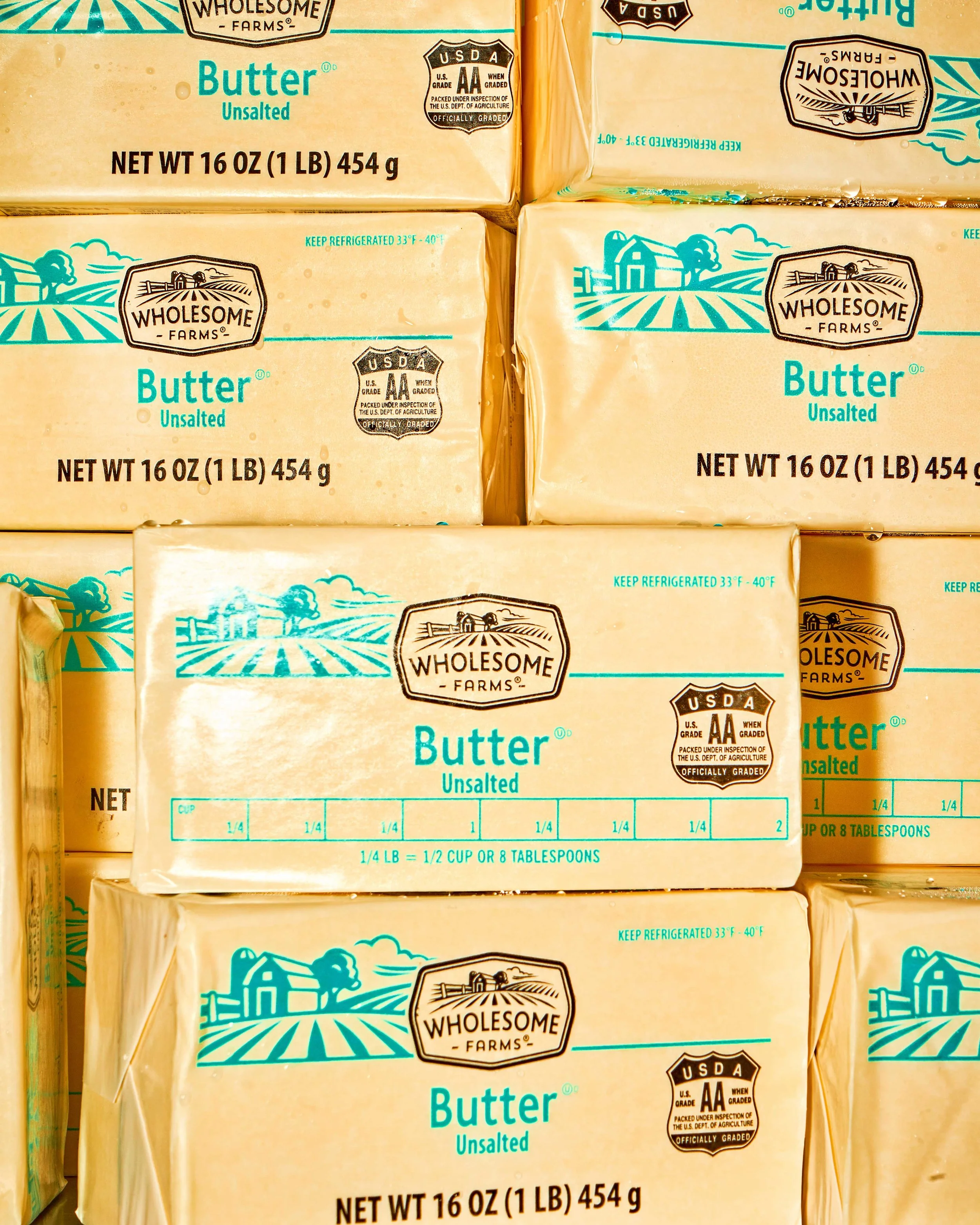 Several packages of Wholesome Farms unsalted butter stacked together with blue and black printing on yellowish paper labels.