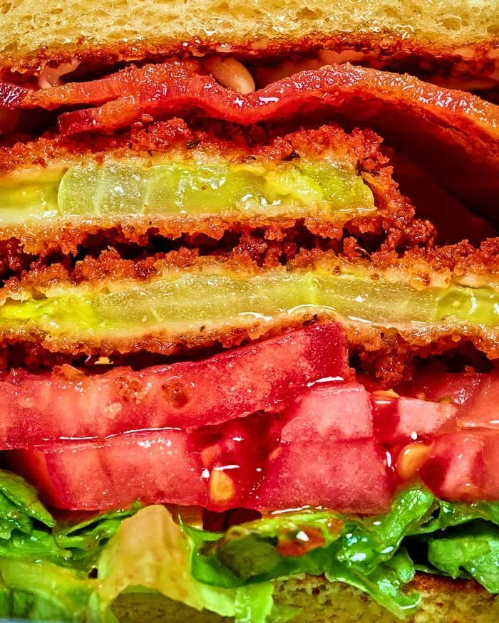 Close-up of a burger with crispy fried patty, sliced pickles, fresh tomatoes, and lettuce.