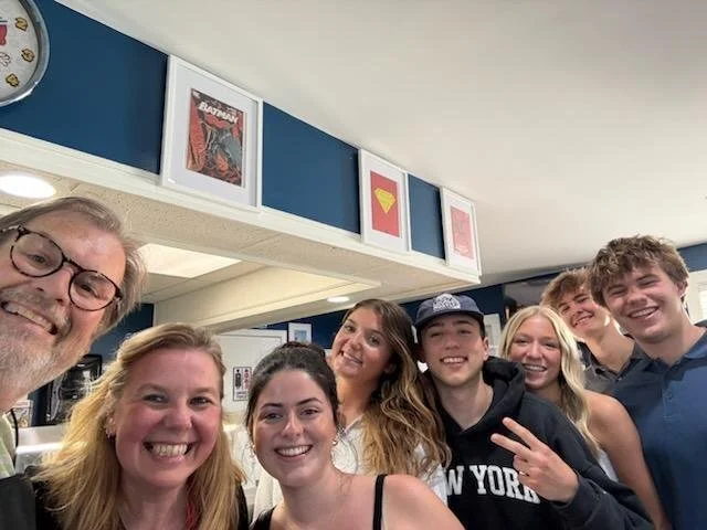 Chuck and Bev sharing a group selfie with a crowd of young men and women, everyone smiling and posing inside Trekker's Nacho Average.