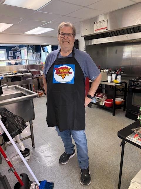 Chuck smiling for a picture in the restaurant's kitchen, wearing an apron with Trekker's logo printing on it.