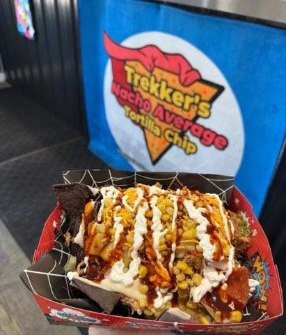 A bowl of nachos loaded with corn, sour cream, and BBQ sauce on a bed of Trekker's Blue Chips.