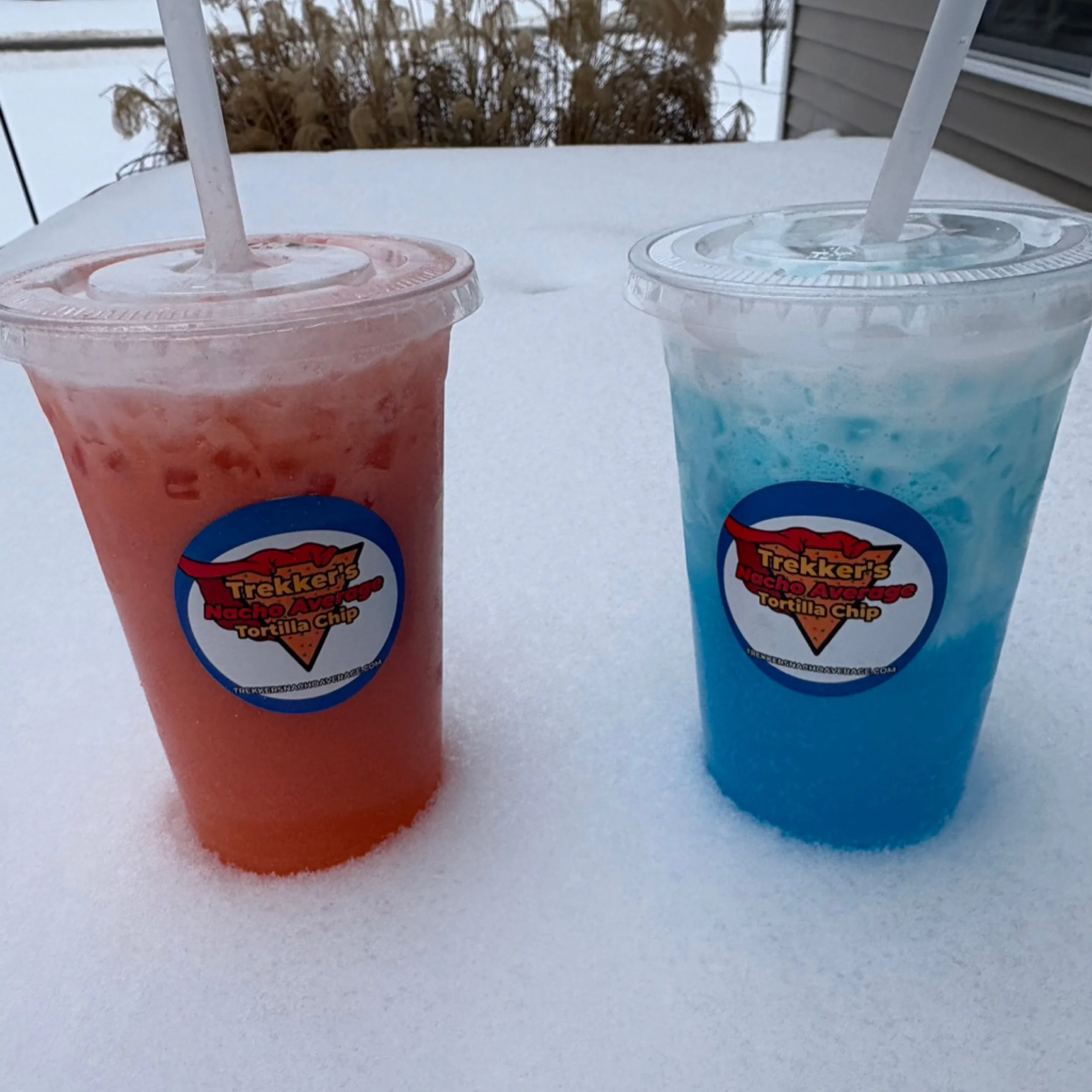 Two iced Trekker's Nacho Average Tortilla Chip drinks, one bright pink and one vibrant blue, sitting in fresh snow.