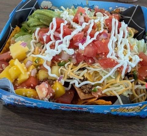 A fruity bowl of nachos including sour cream, pineapple, tomatoes, shredded cheese, and onions on a bed of nacho chips.