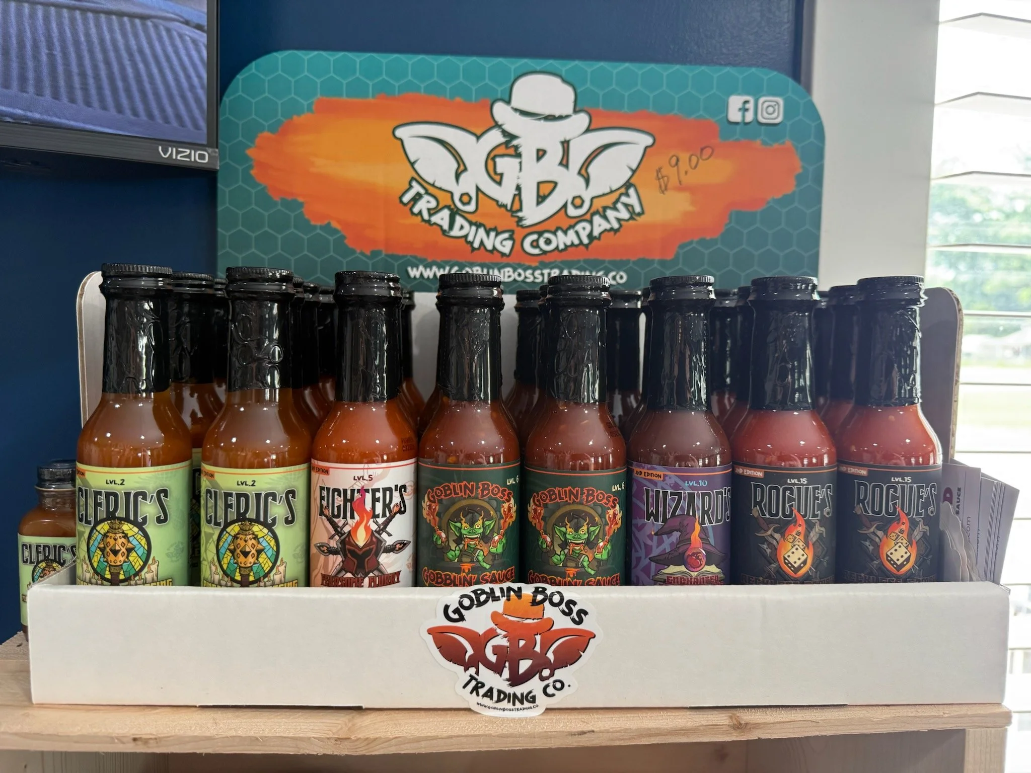 An array of various hot sauces provided by Goblin Boss Trading Company sitting in an open box on a shelf.