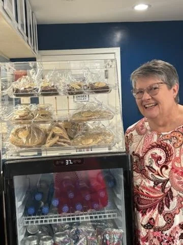 Chuck's sister smiling next to the cookie shelf and cooler.