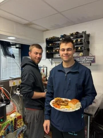 Chuck and Bev's sons working the kitchen with smiles and one holding a plate of snacks.