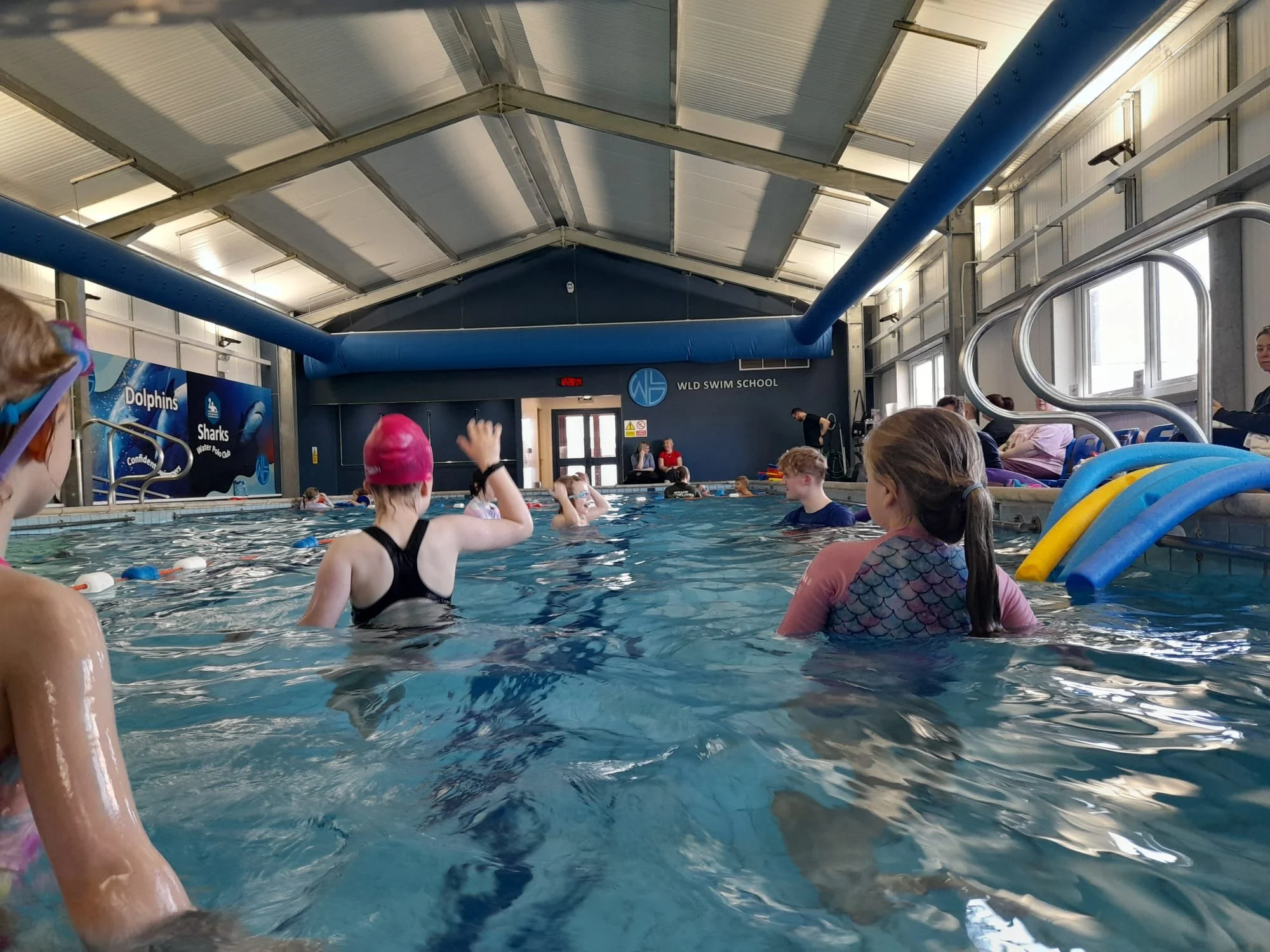 Children and adults in an indoor swimming pool during a swim class or training session at WLD Swim School.