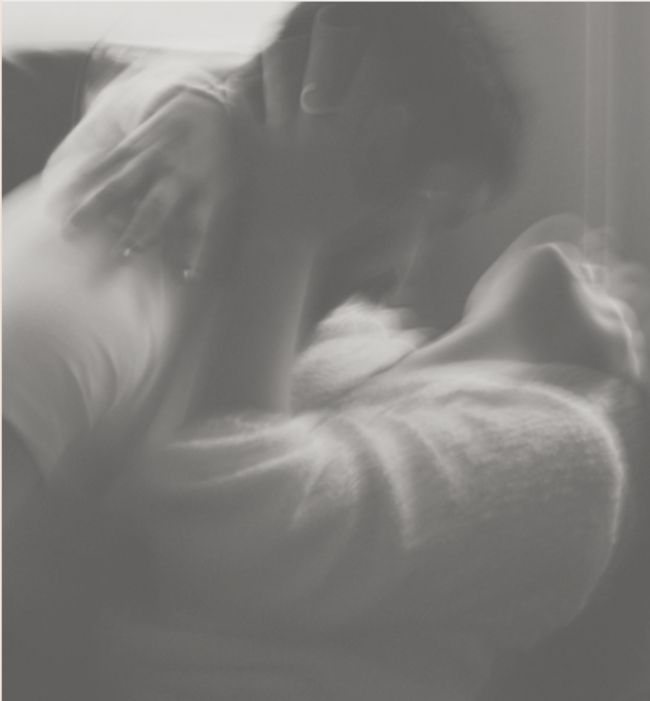 Soft-focus black-and-white image of two partners laughing and embracing while leaning on one another.