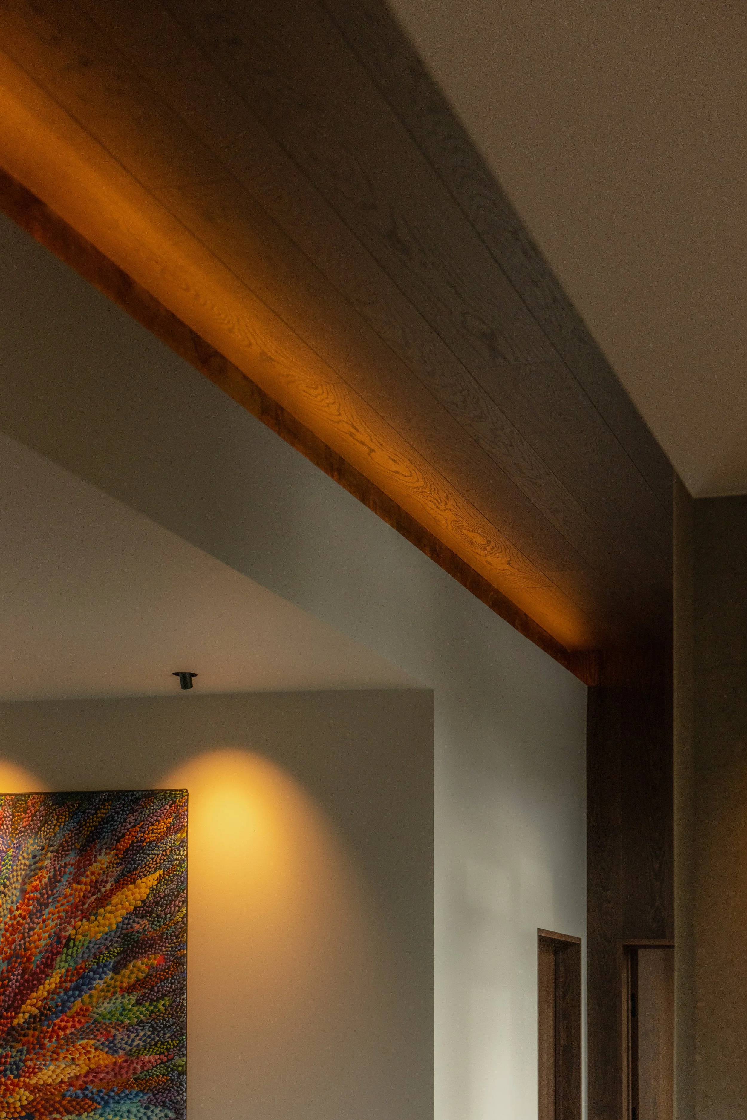 Interior view of a room with dark wooden ceiling and trim, colorful artwork on a wall, and a light fixture.