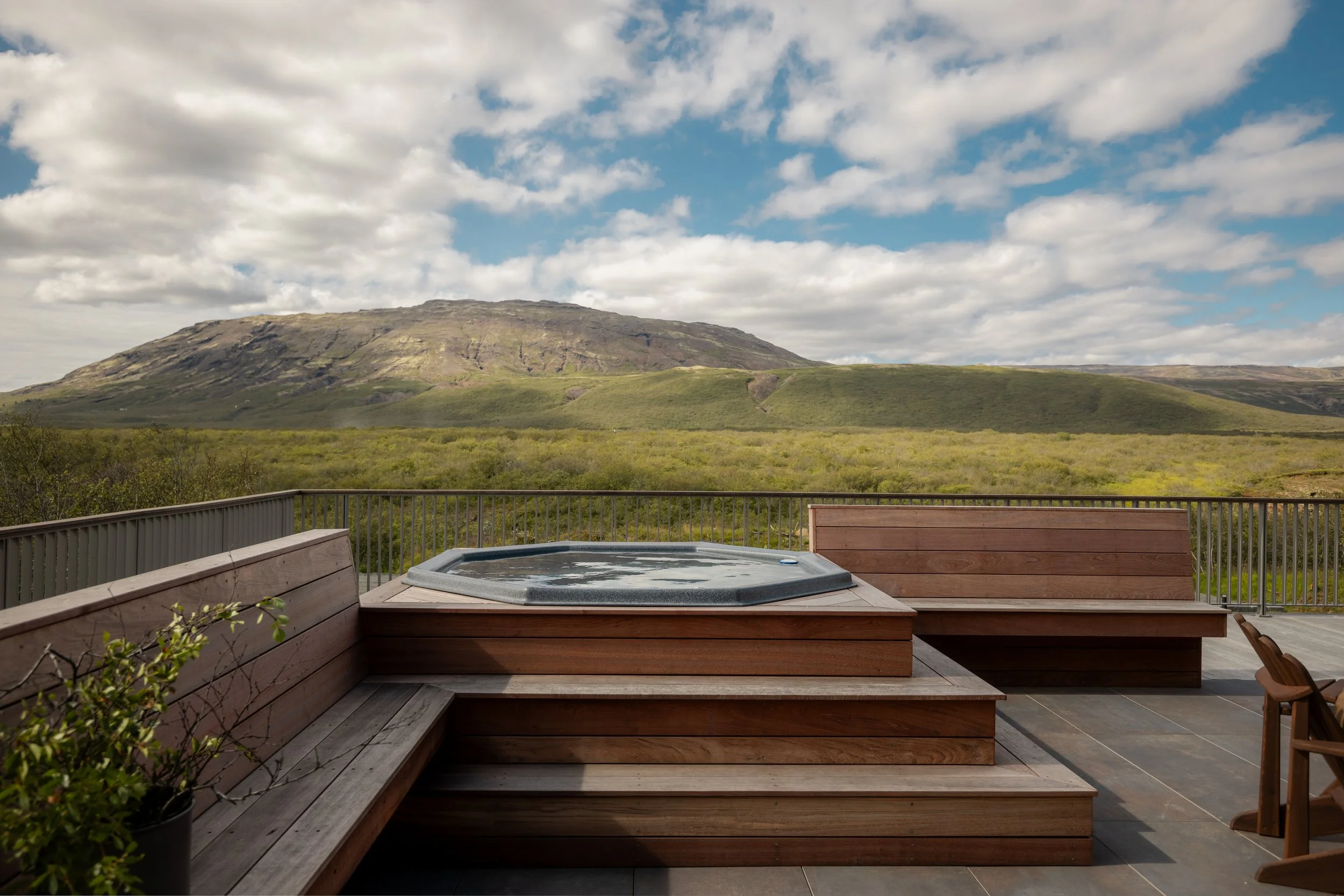Outdoor deck with a hot tub and a view of a mountain and cloudy sky in the background.