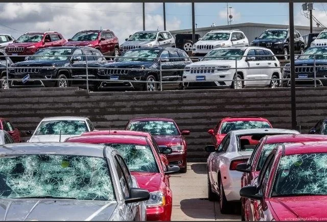 Multiple cars in a dealership lot, some with cracked windshields, arranged in rows with a mix of colors including red, black, white, and gray.