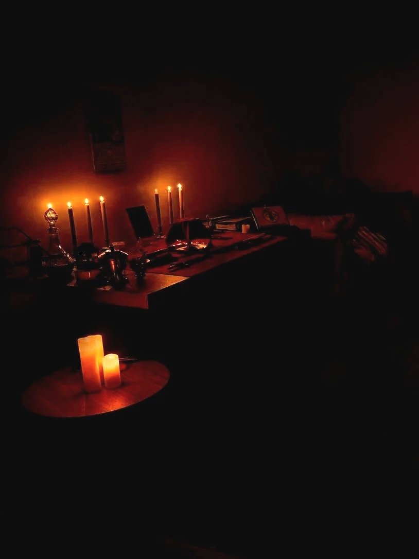 Dimly lit room with candles on a table and a desk, creating a cozy ambiance.