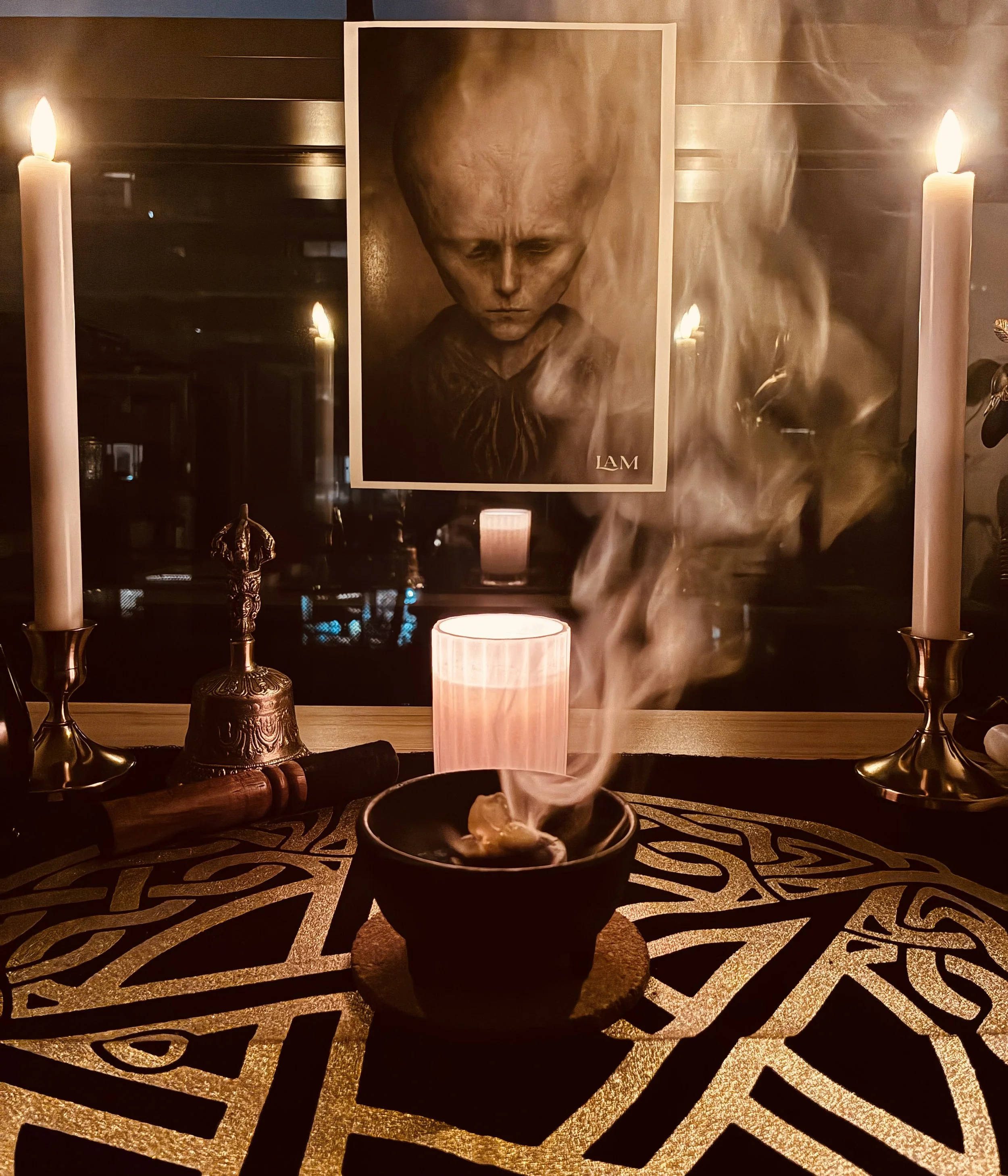 A photograph of a memorial setup with candles, incense, and a smoke-filled bowl on a decorated table. In the background, there is a portrait of a person with a somber expression surrounded by smoke.