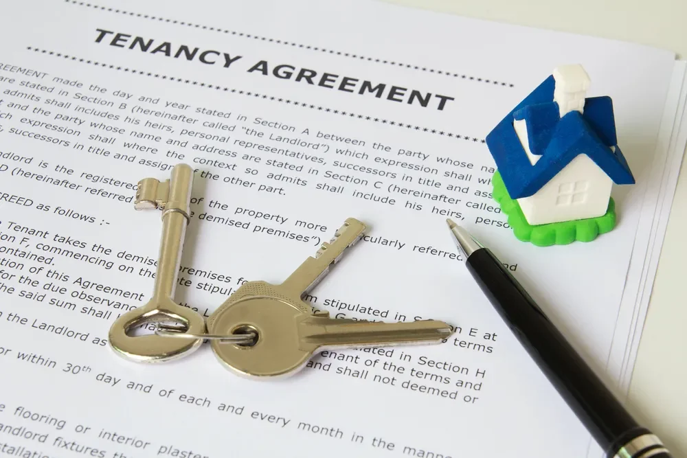 A document titled 'Tenancy Agreement' with a set of keys, a small house figurine, and a pen on top of the paper.