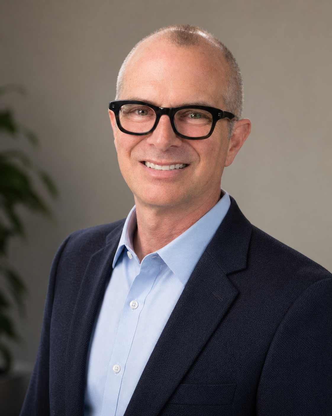 Headshot of a middle-aged man with glasses, dressed in a dark blazer and light blue shirt, smiling against a neutral background.
