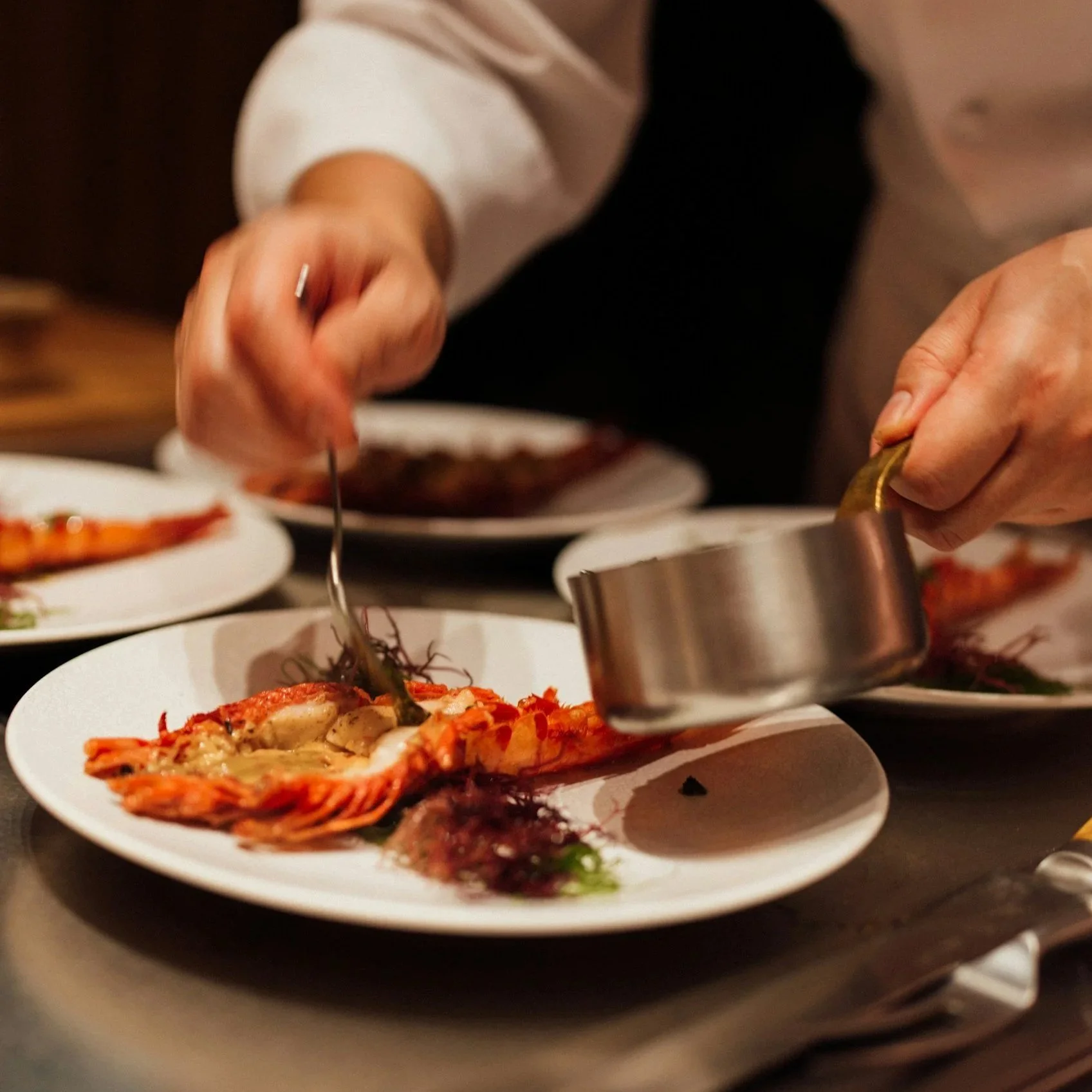 Chef plating a lobster dish in a restaurant kitchen.