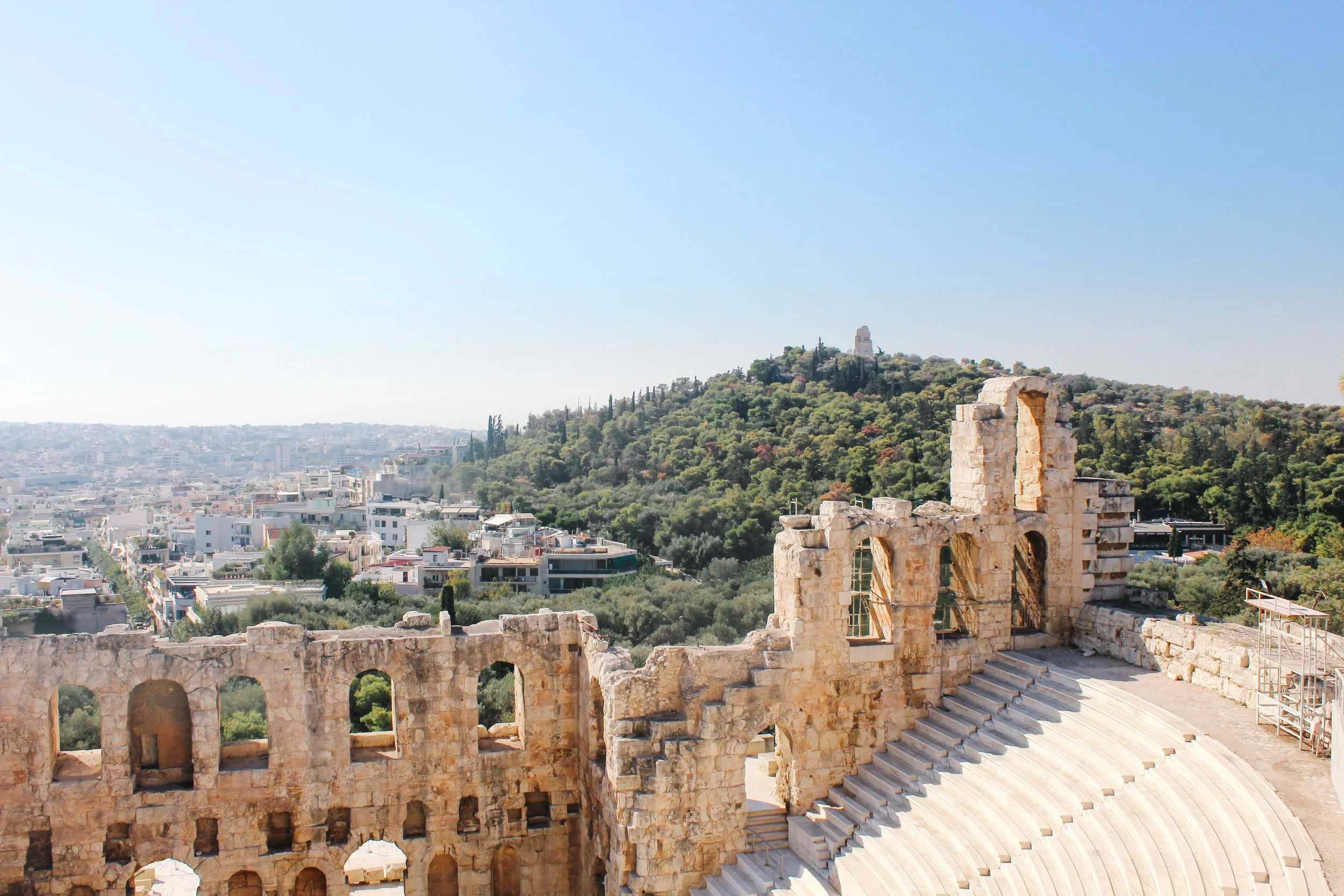 Ancient stone ruins of a historical theater in Ephesus, Turkey, with a desert-like cityscape and green hill in the background.