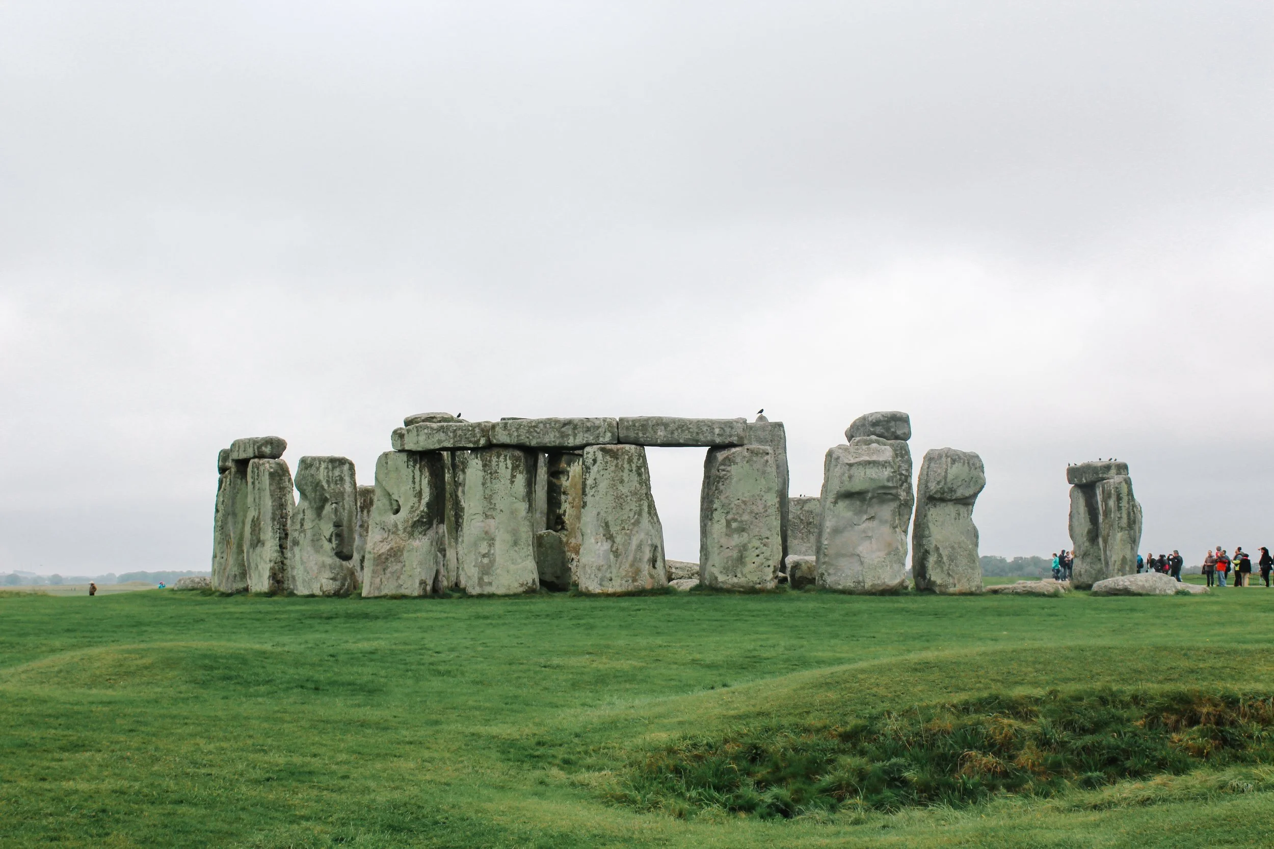 Stonehenge, a prehistoric monument in England, with large standing stones arranged in a circular layout and a group of tourists nearby on a cloudy day