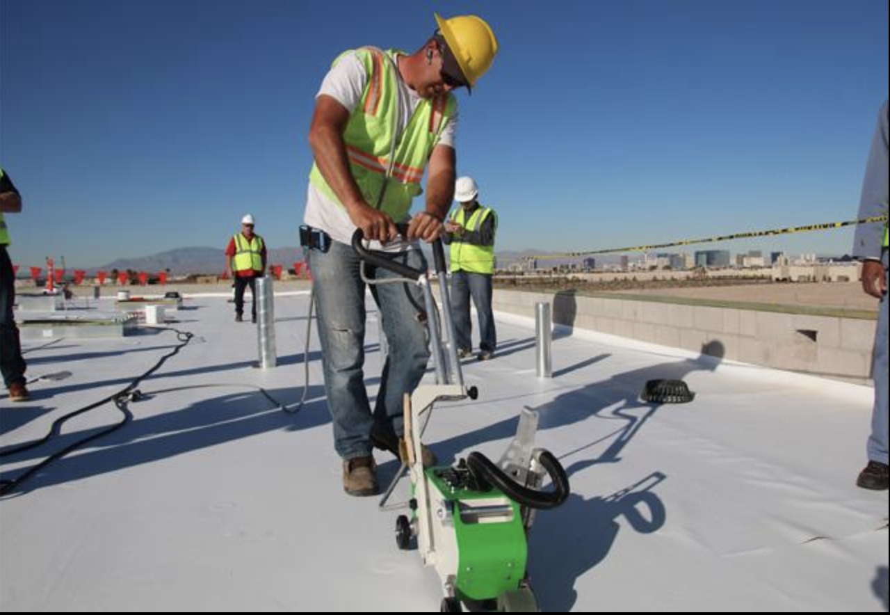 Construction workers wearing safety vests and helmets on a building rooftop, using a laser leveling device for construction.